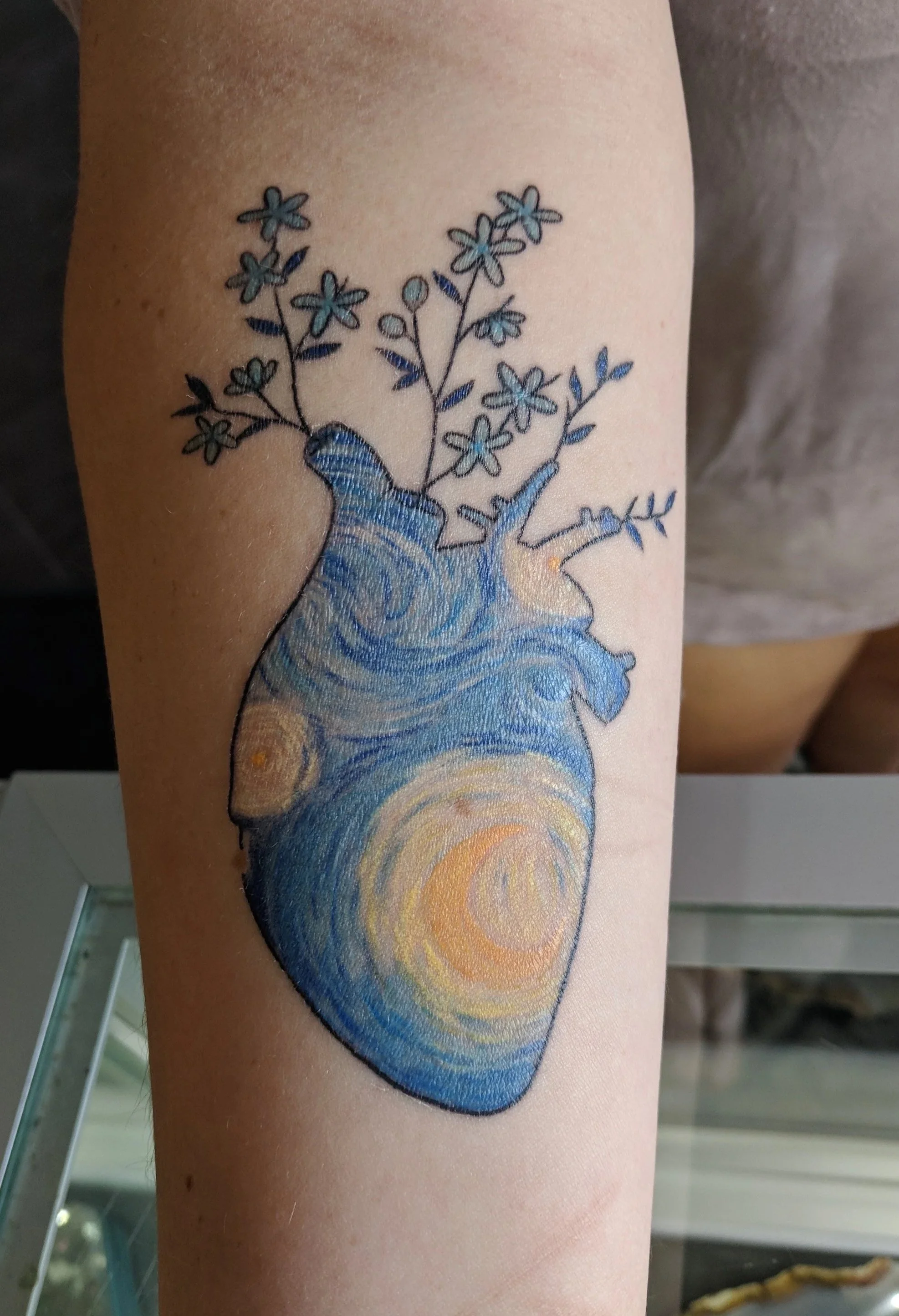 Tattoo of a colorful, artistic heart with flowers sprouting from the top.