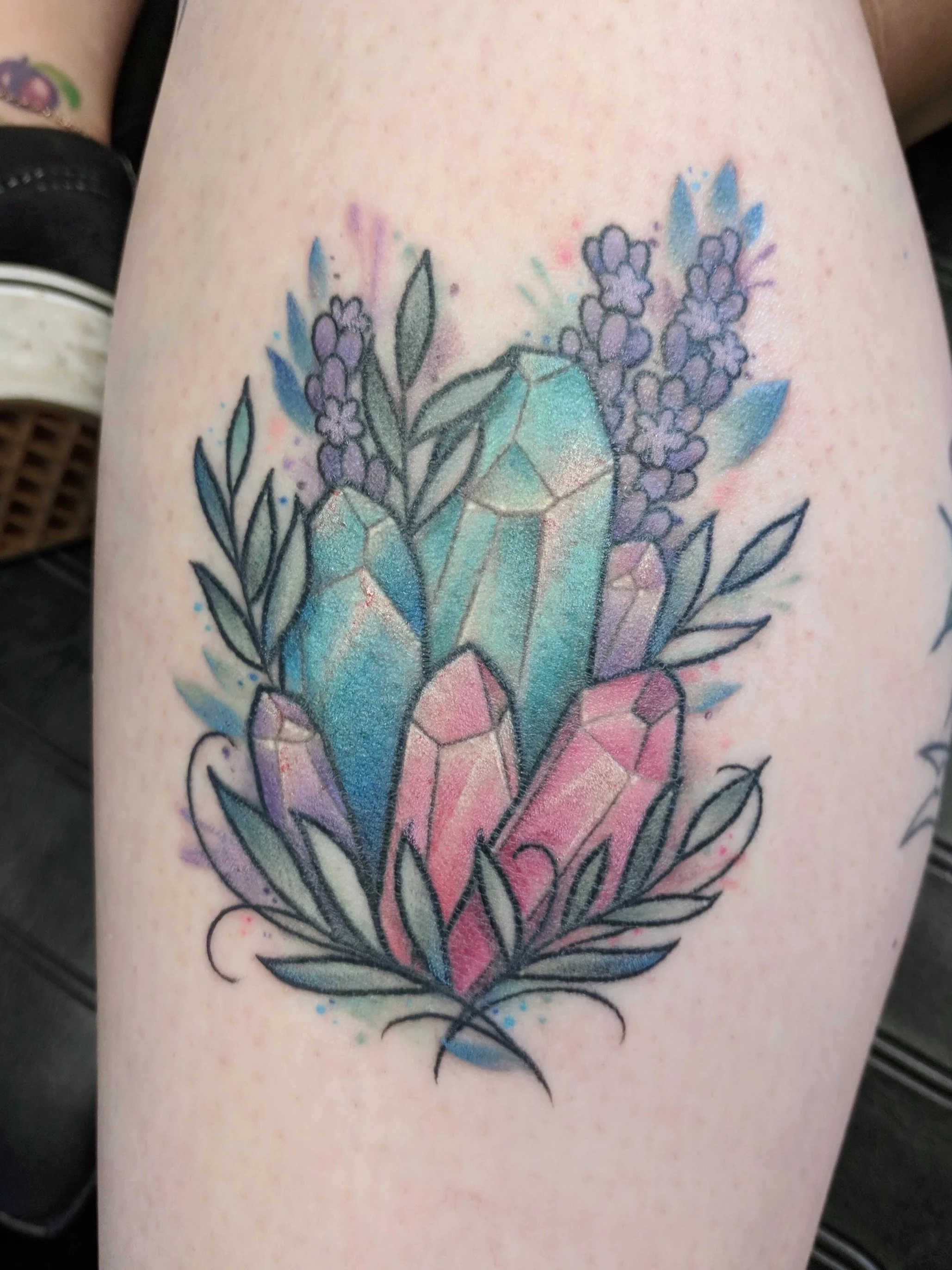 Colorful tattoo of crystals and lavender flowers on person's thigh with black outlines and watercolor-style shading.