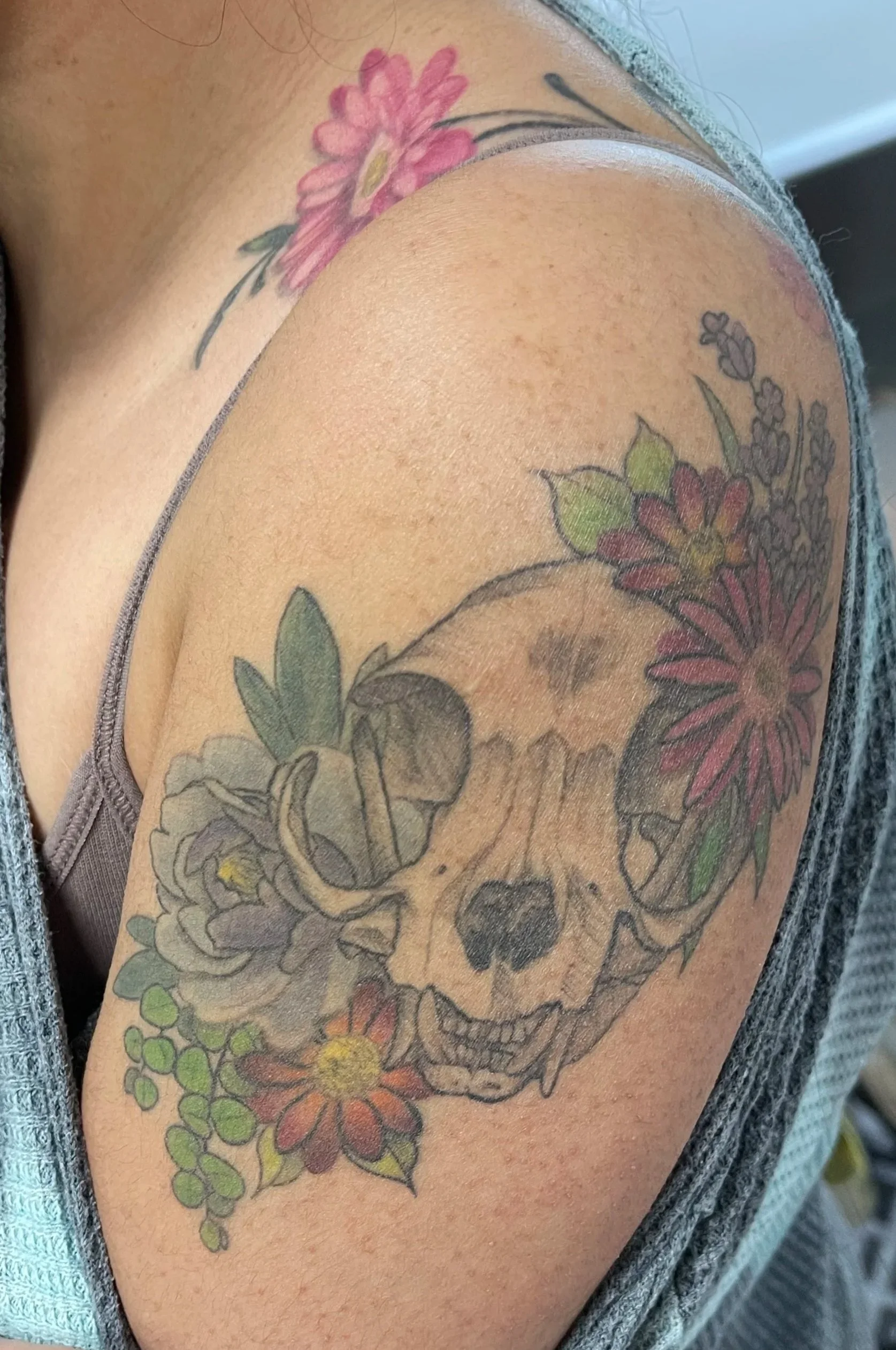 Tattoo of a skull with flowers around it on person's upper arm.
