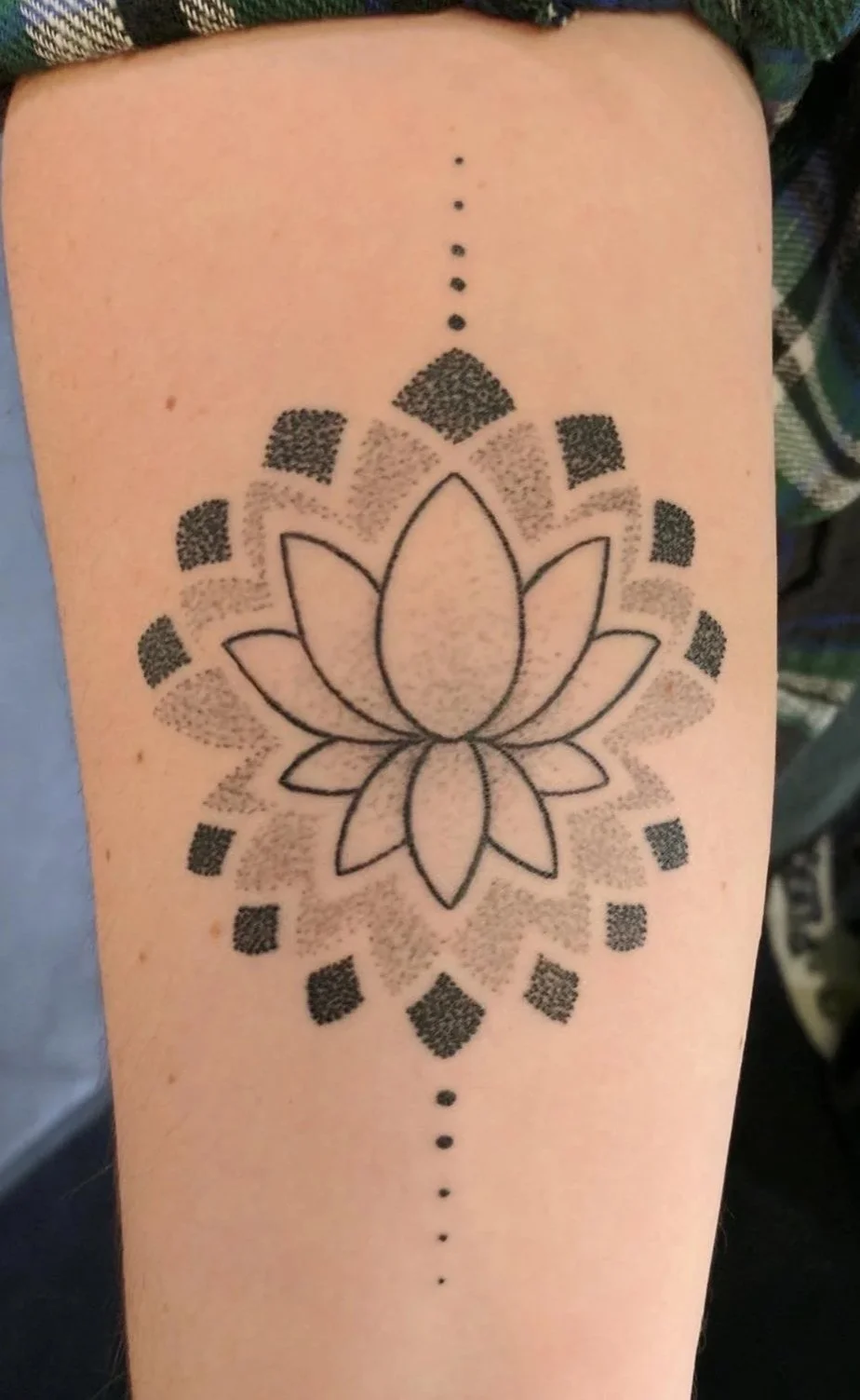 Tattoo of a lotus flower with geometric patterns and dotted lines on inner forearm.
