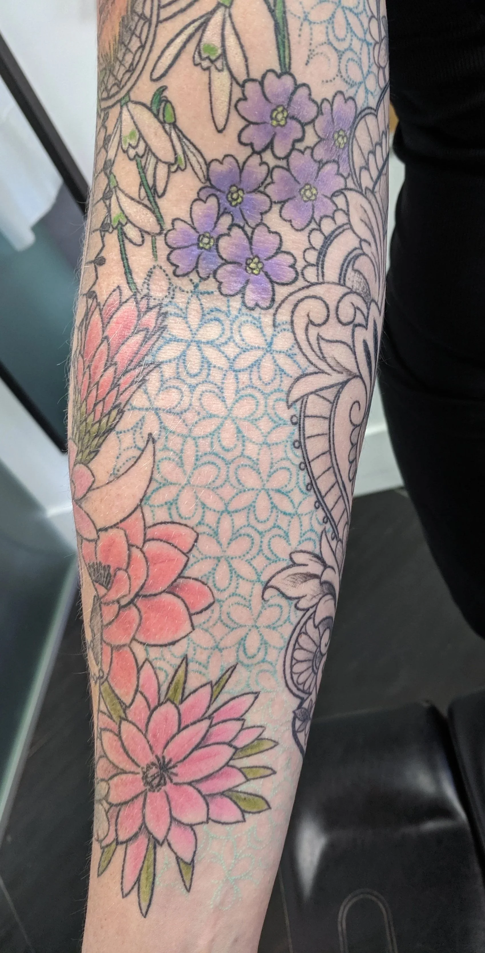 Tattooed arm with purple and pink flowers and intricate blue patterns.