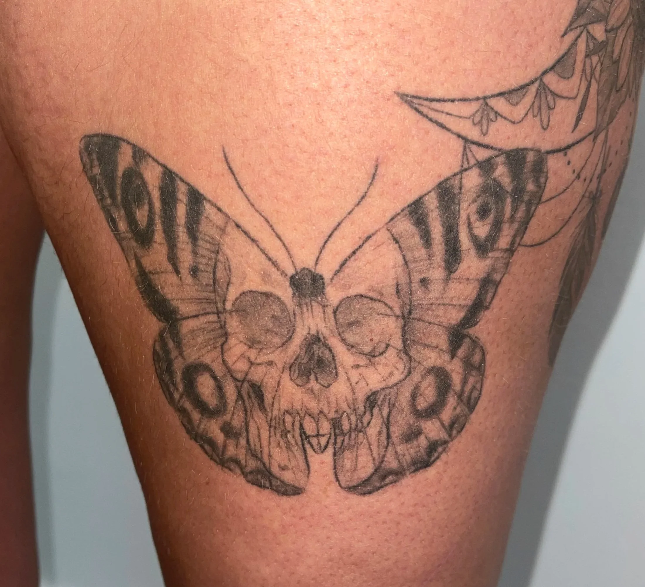 Tattoo of a butterfly with a skull at its center on a person's thigh