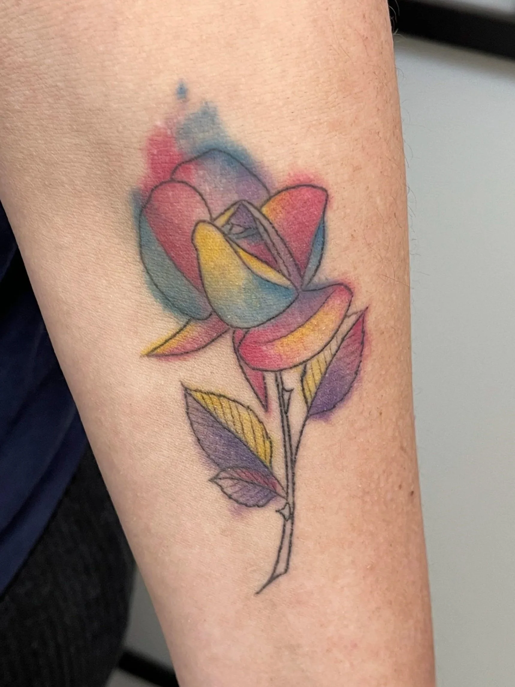 Colored tattoo of a rose with a watercolor background on a person's arm.