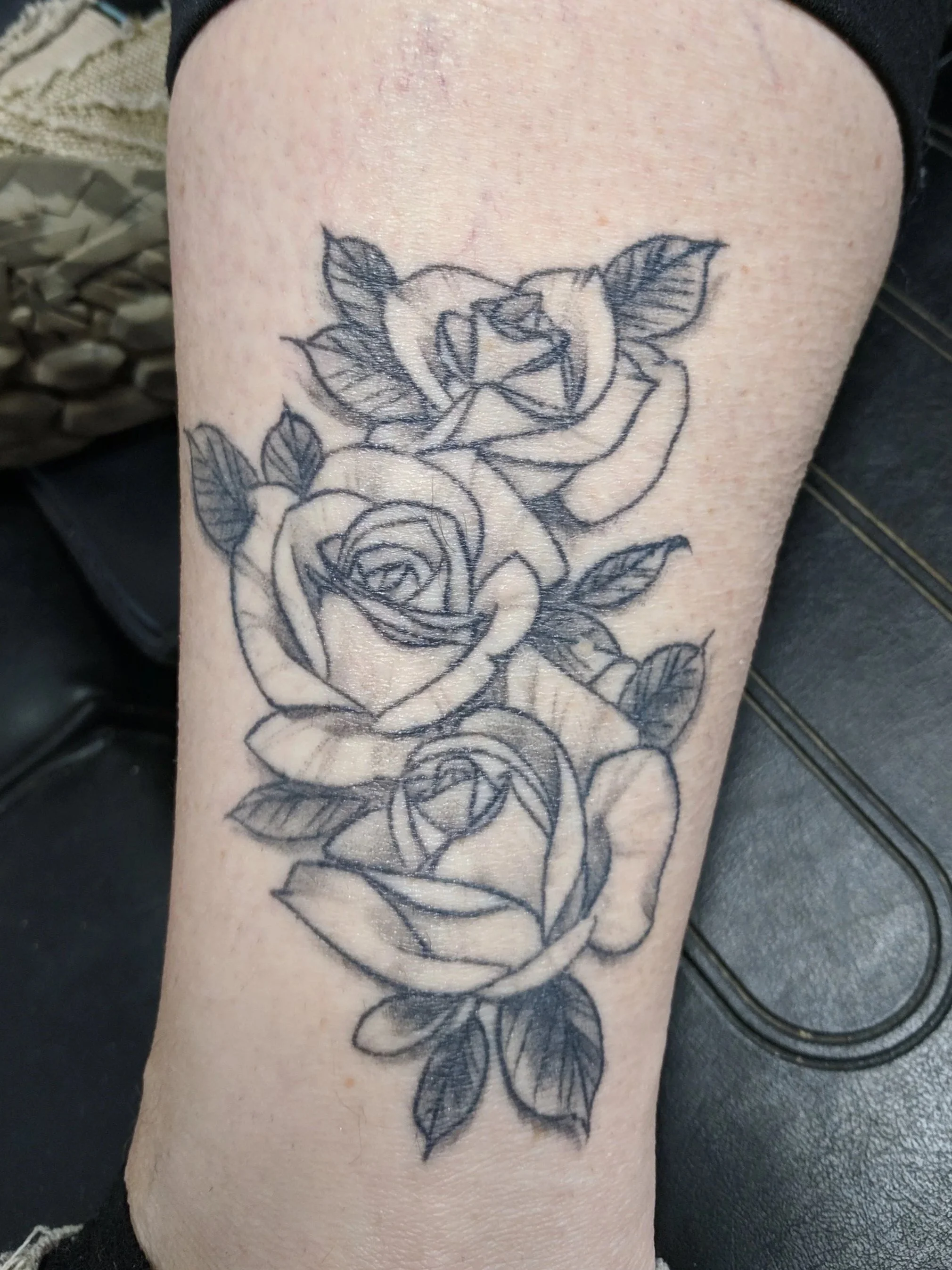 Black and gray tattoo of three roses with leaves on a person's leg.