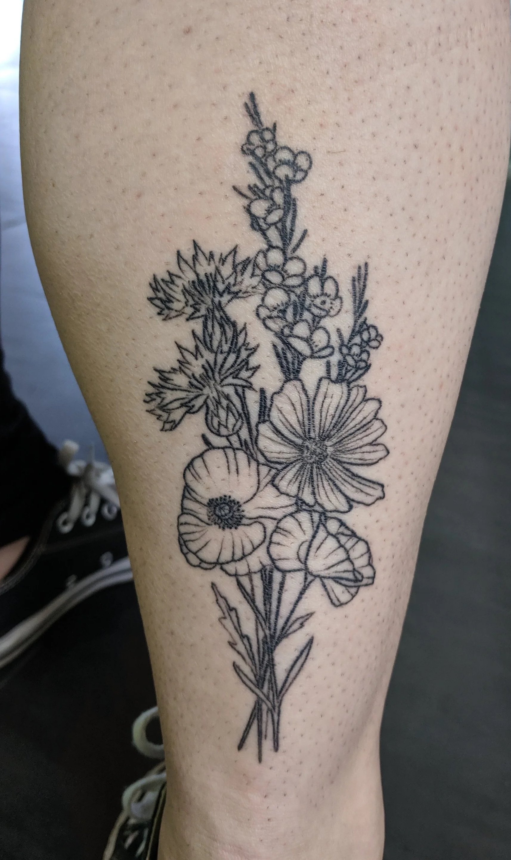 Black line tattoo of a flower bouquet on a person's lower leg.
