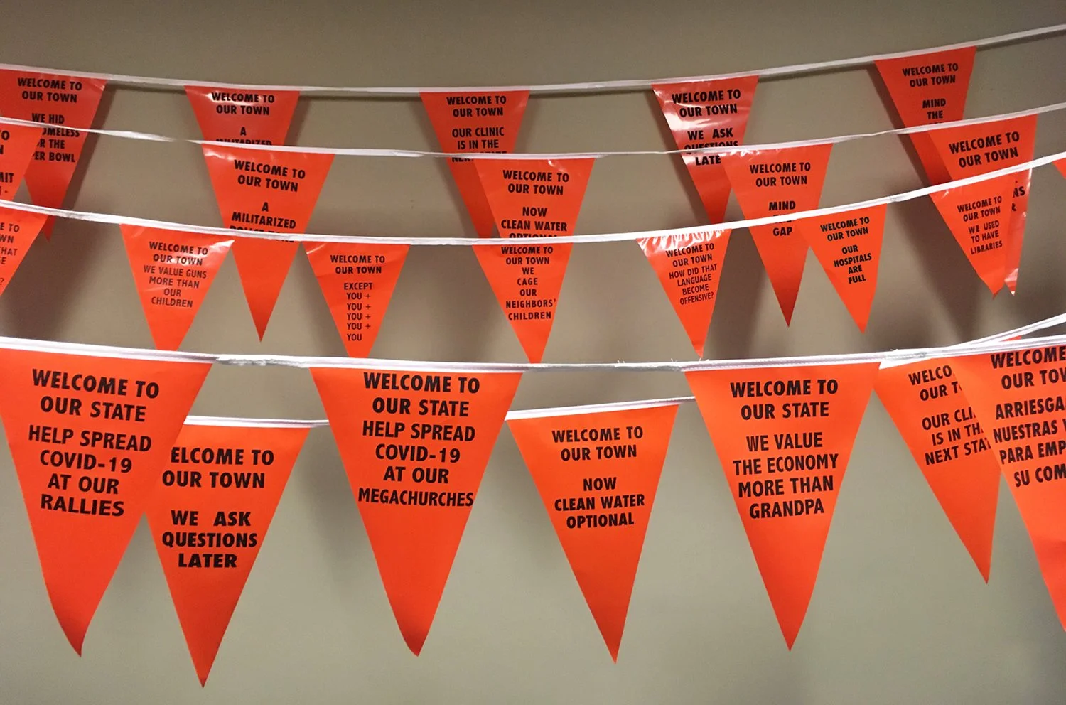  Orange screenprint plastic pennants. Installation view detail. This iteration featured problematic responses to the COVID pandemic. 