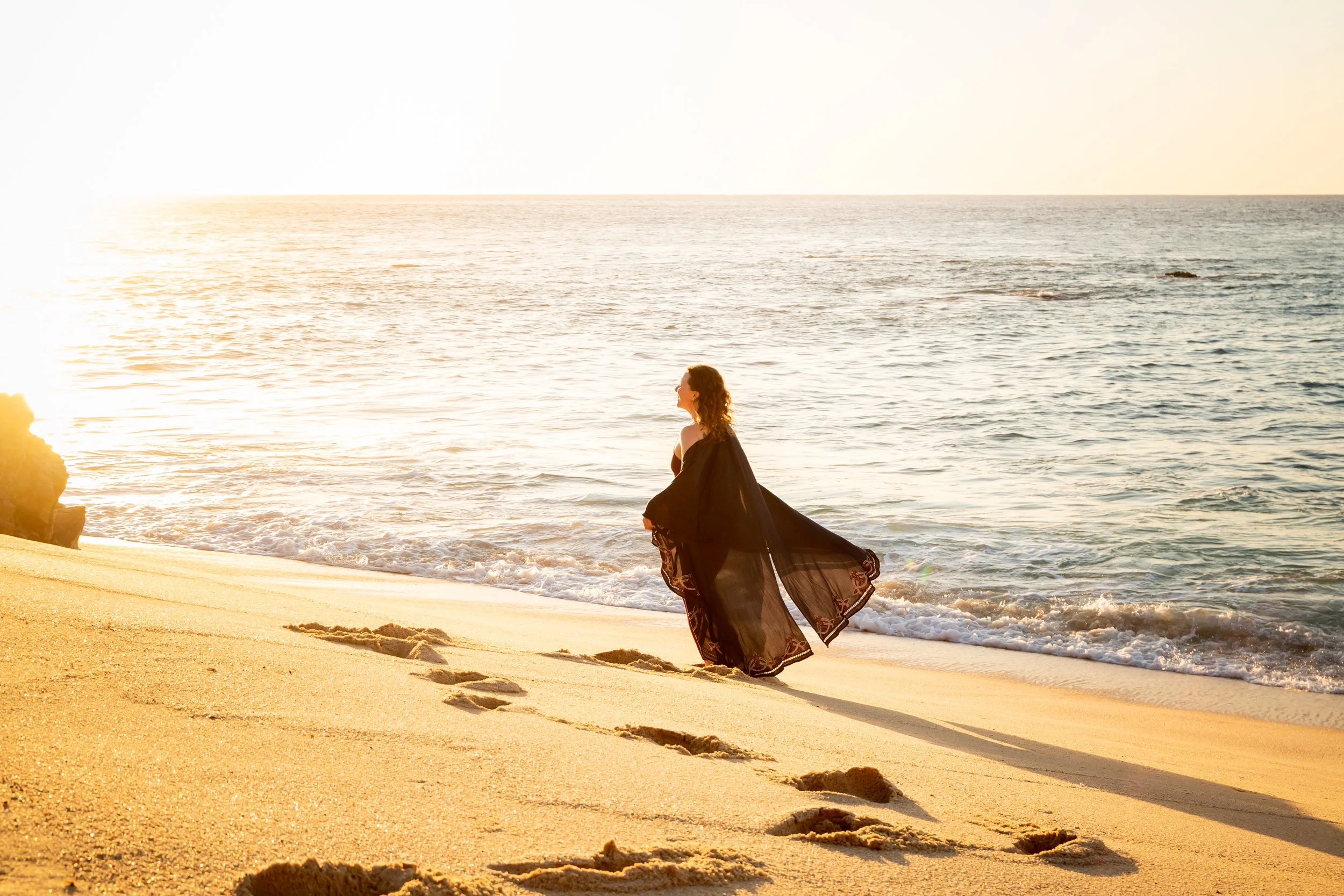 Sarah Anne wearing a flowing robe while walking on the beach towards the ocean