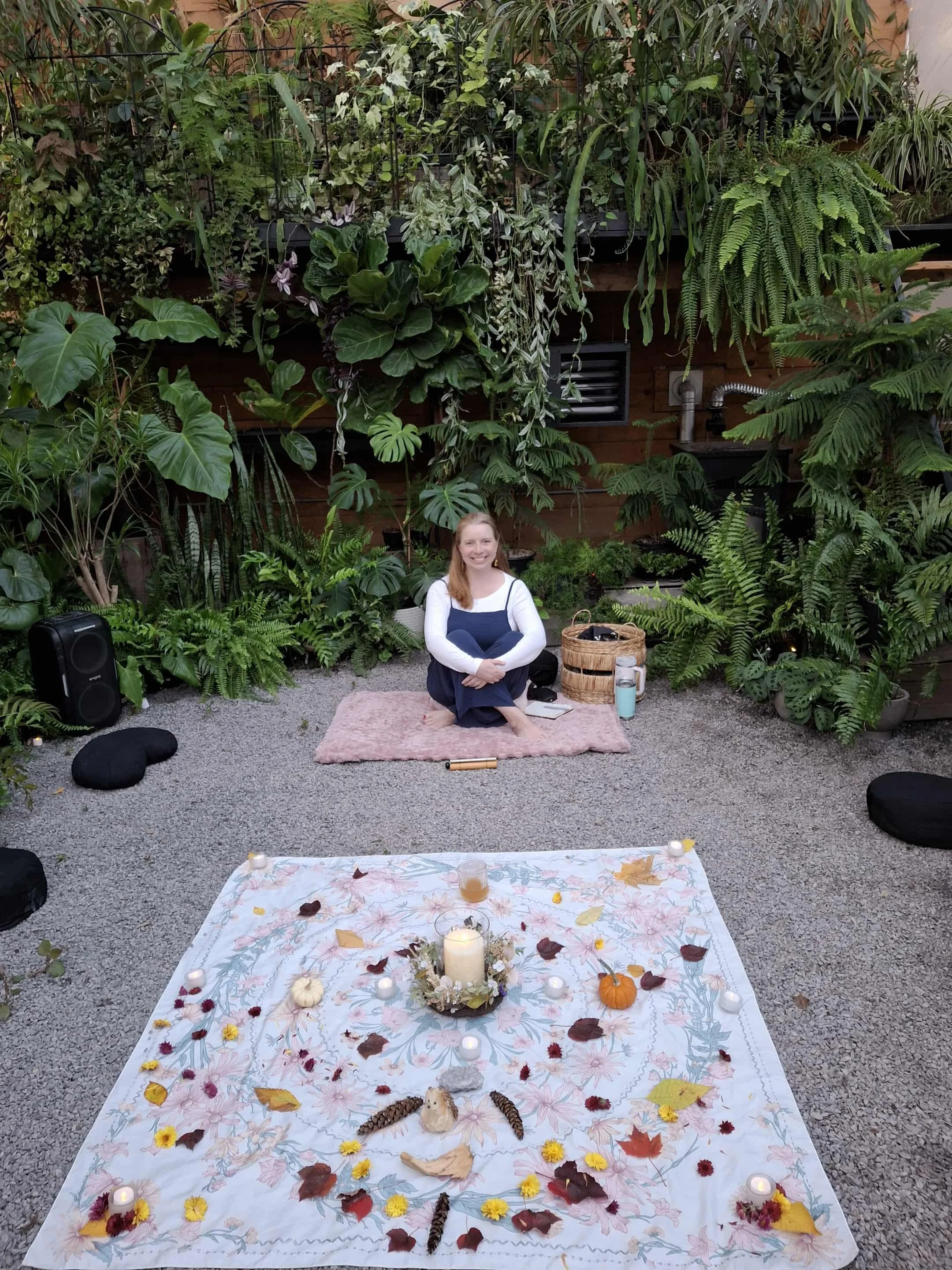 Sarah Kelly sitting in a greenhouse with an altar on the ground on front of her.