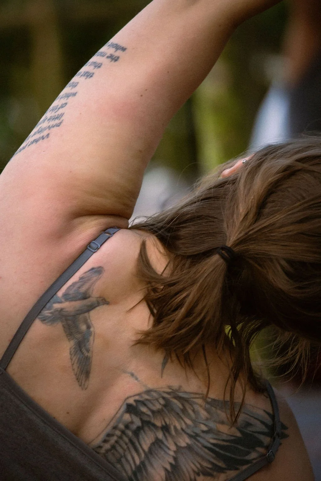 A woman with tattoos does a side bend to the right while sitting.