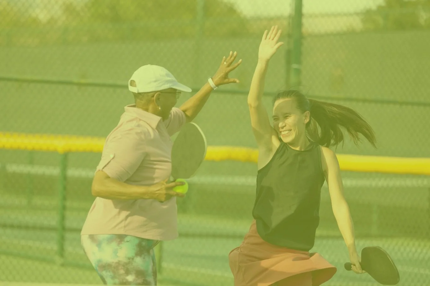 Two women playing pickleball, high-fiving on a court.