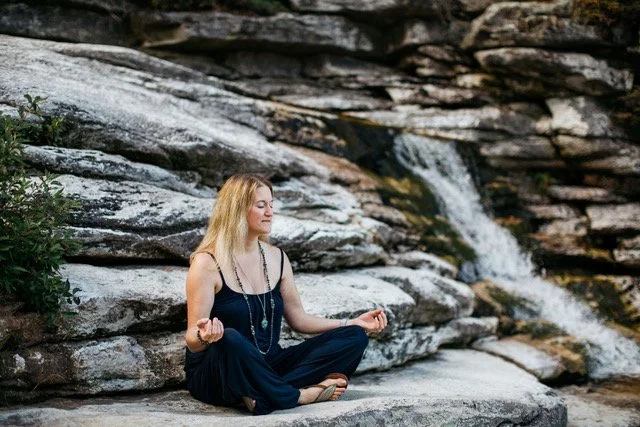 women meditating on rocks in front of a waterfall