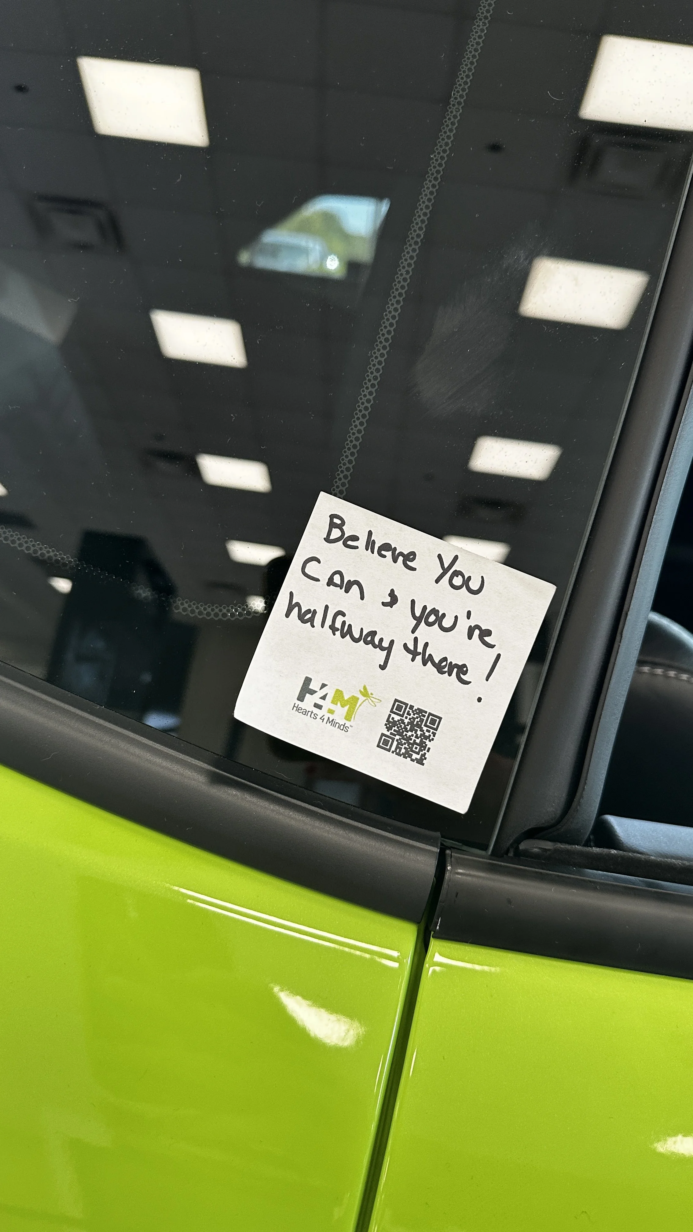 Small sticky note with an inspirational message on it stuck to a car.
