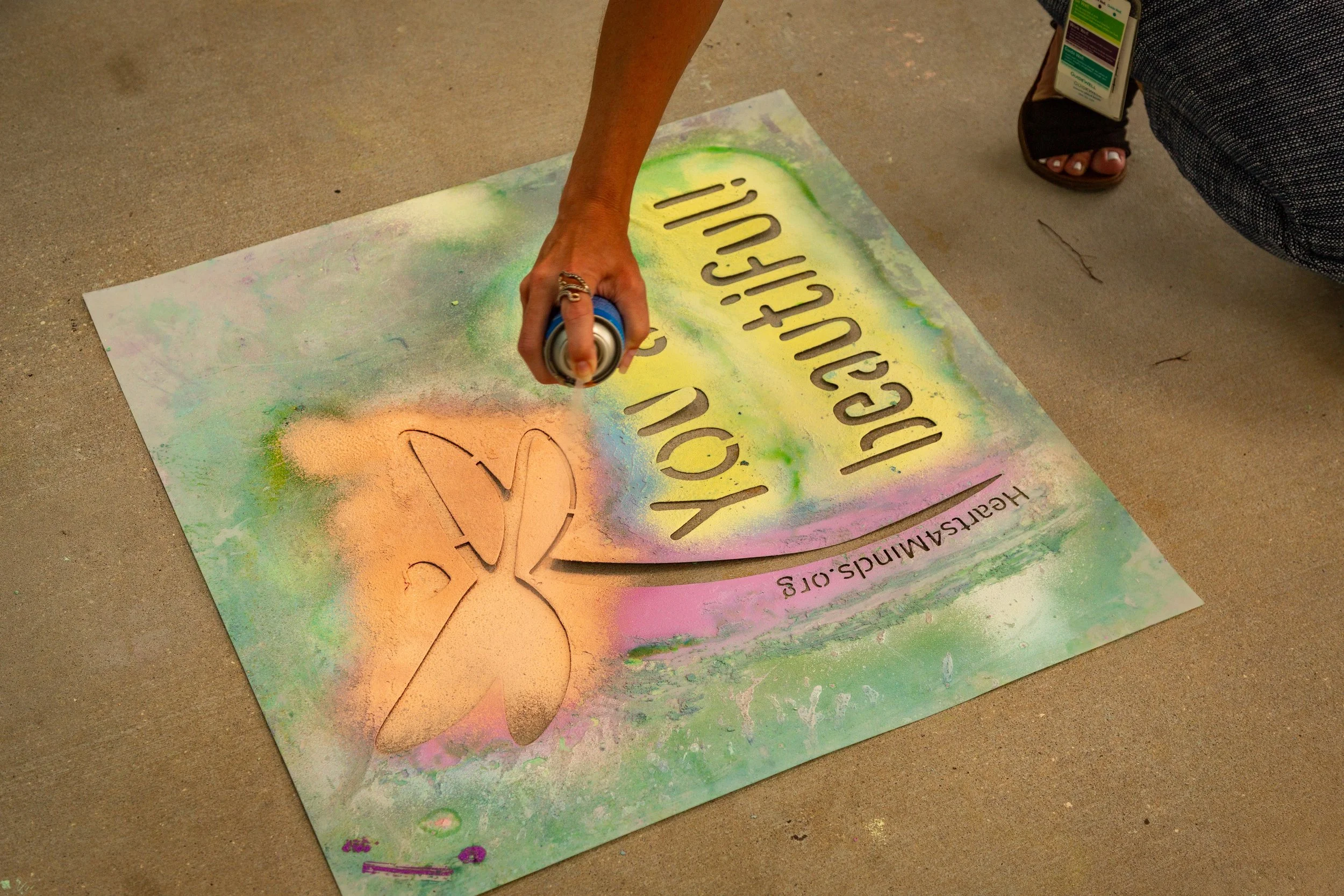 Community member creating mental health awareness art with spray chalk and dragonfly design.