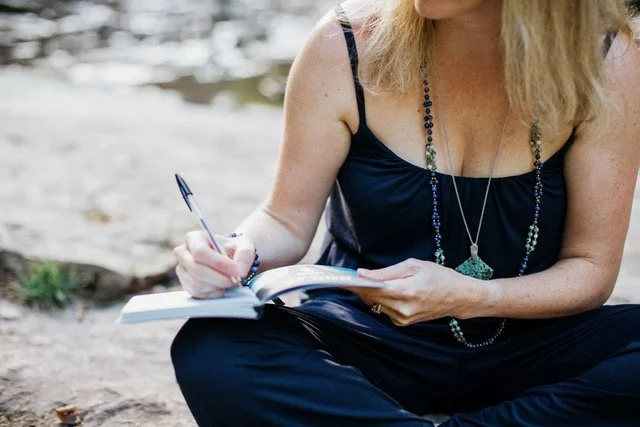 women sitting down outside writing in journal