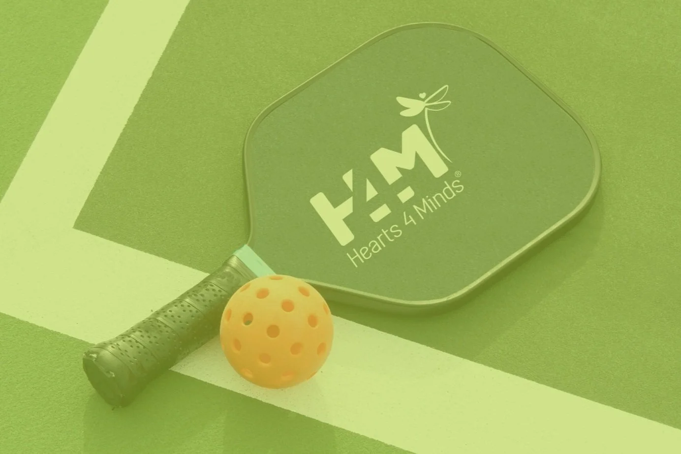 A pickleball paddle labeled "Hearts 4 Minds" resting on a court with an orange pickleball.