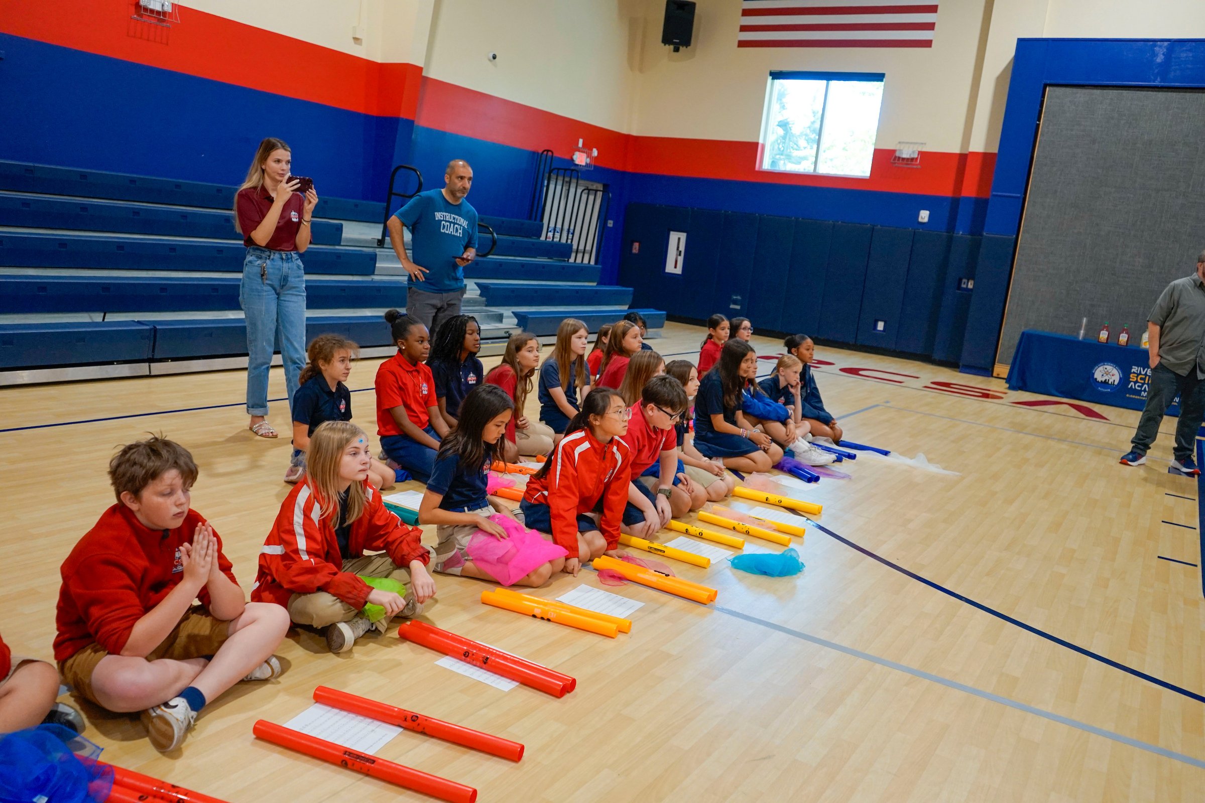 Group of kids sitting on the gym floor with music instruments.