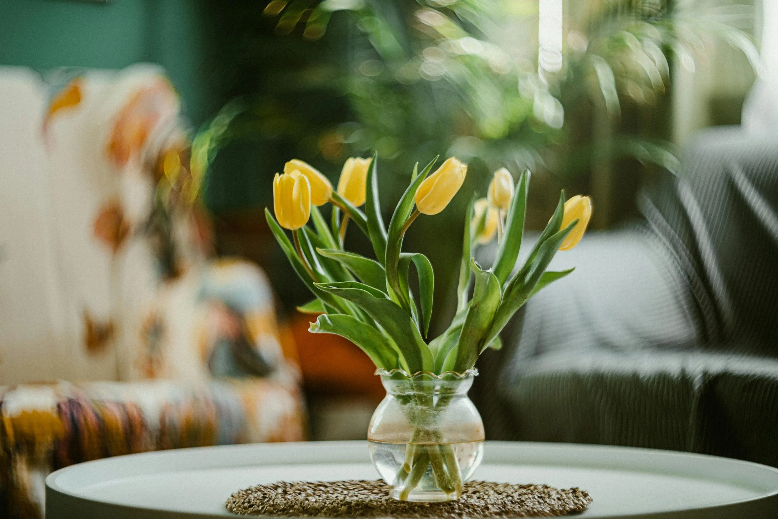 Yellow tulips in a glass vase on a white table inside a home.