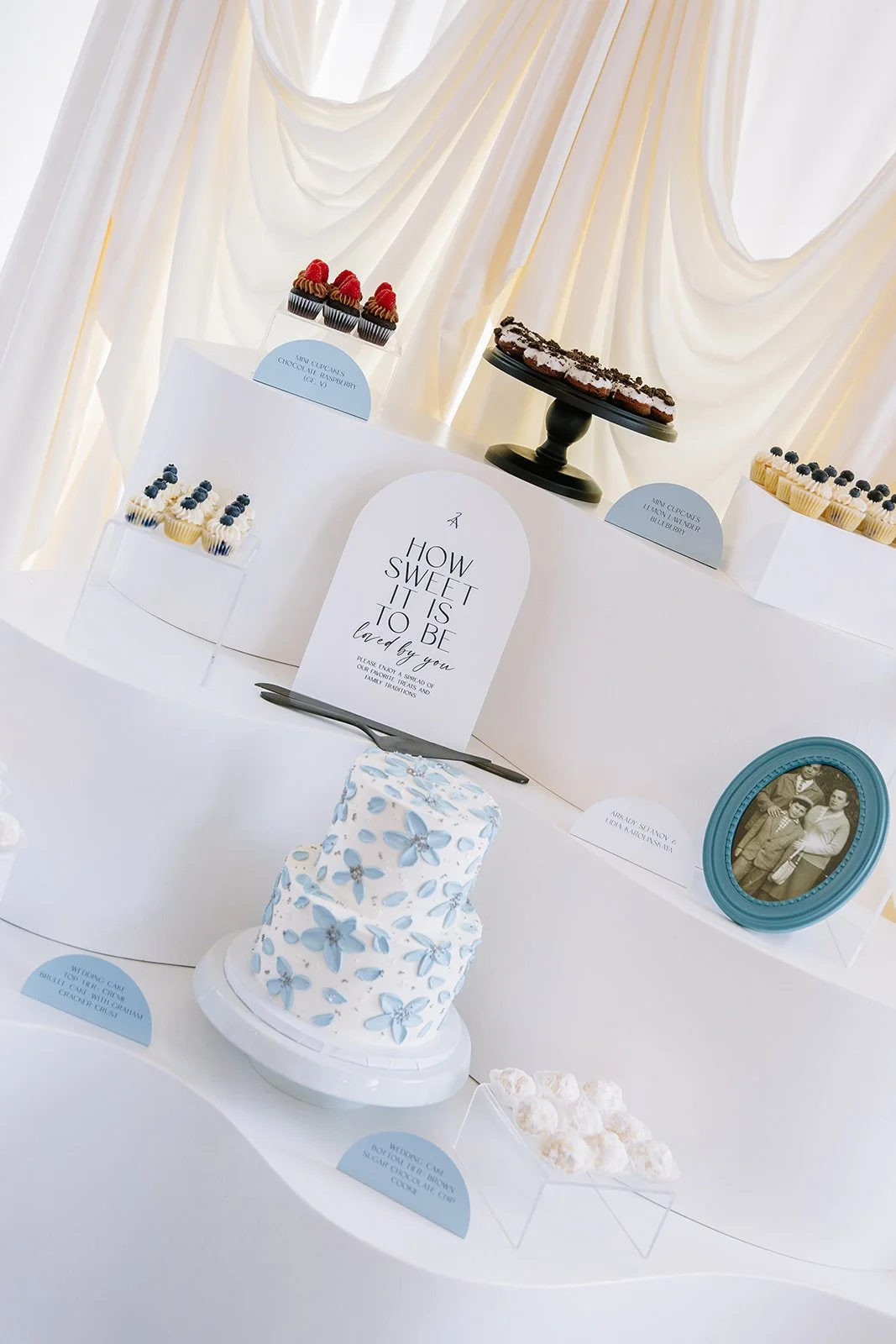 a unique wedding day dessert display with a two-tier blue and white floral cake and cute cupcakes
