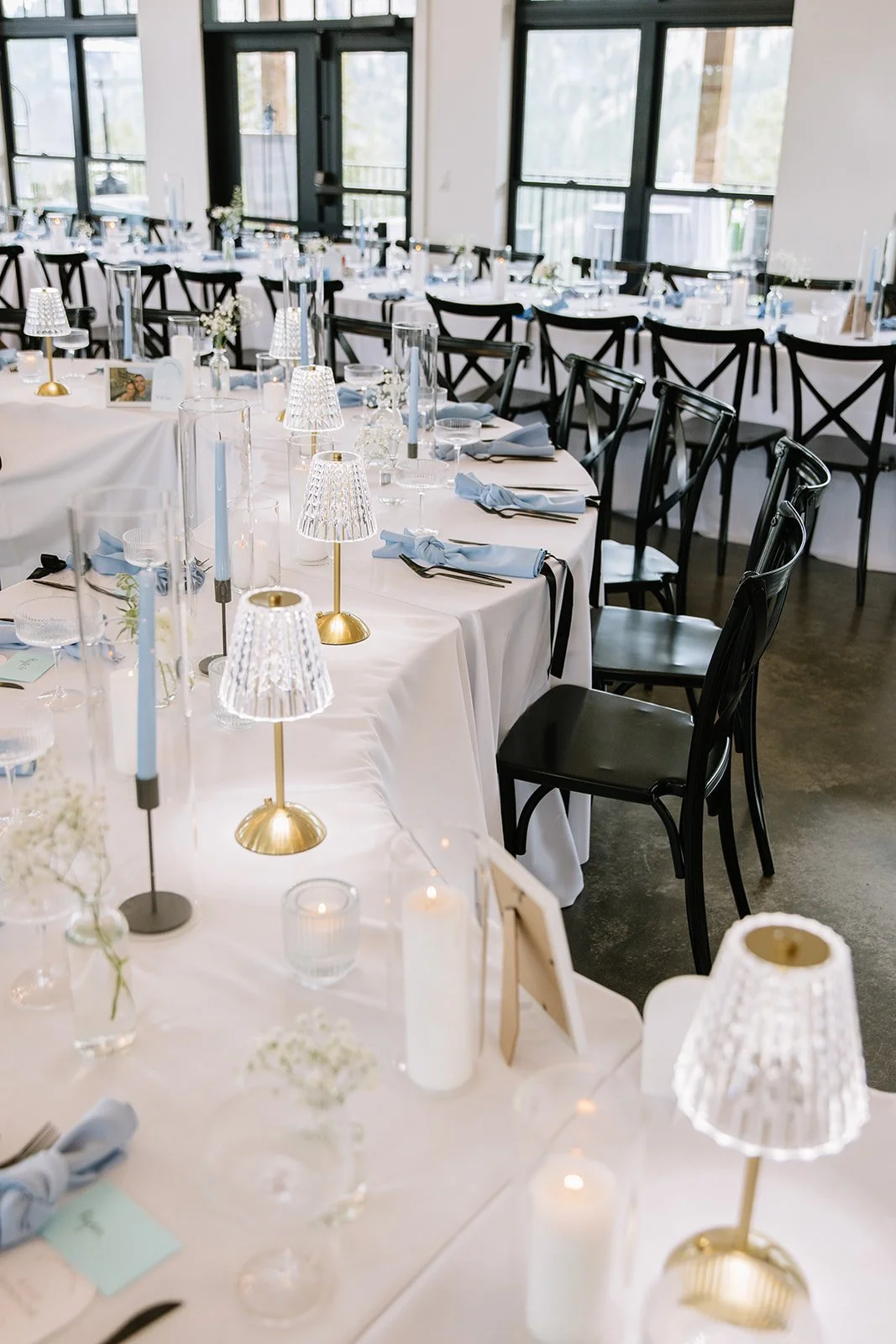 Wedding reception table with glass lamps and candles. Blue napkins and taper candles line the table as well