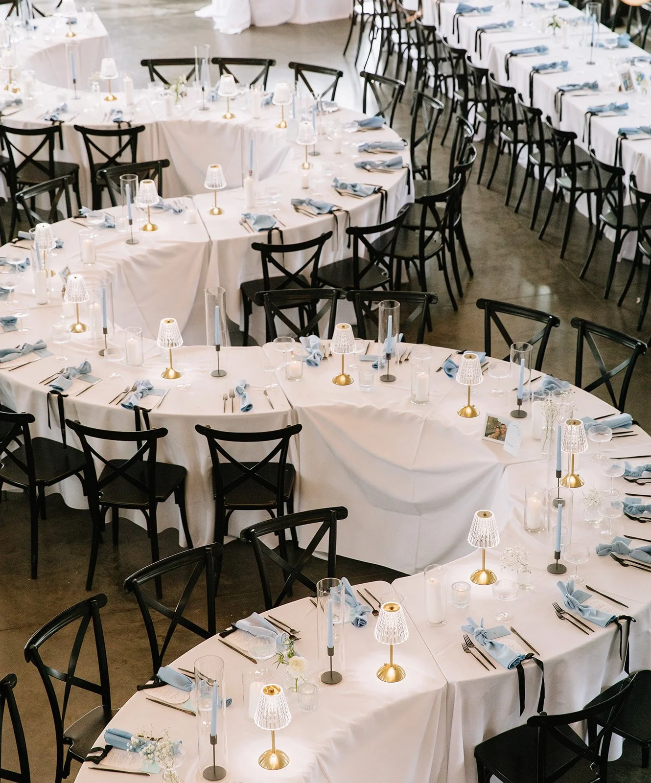 serpentine wedding tables in a modern venue with white linen tablecloths and lamps on the tables