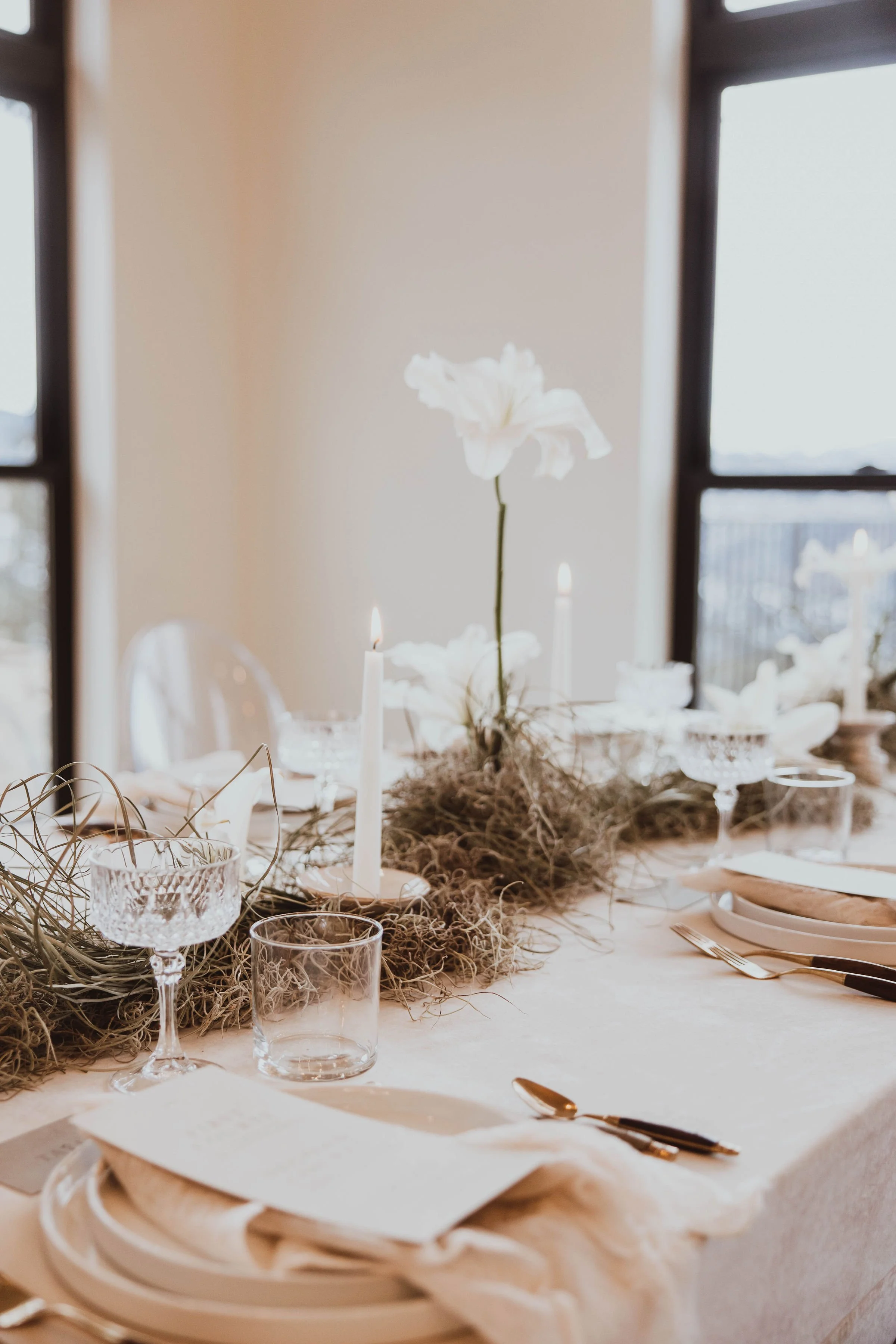 Elegant dining table decor with white flowers, candles, and glassware set for a formal occasion.