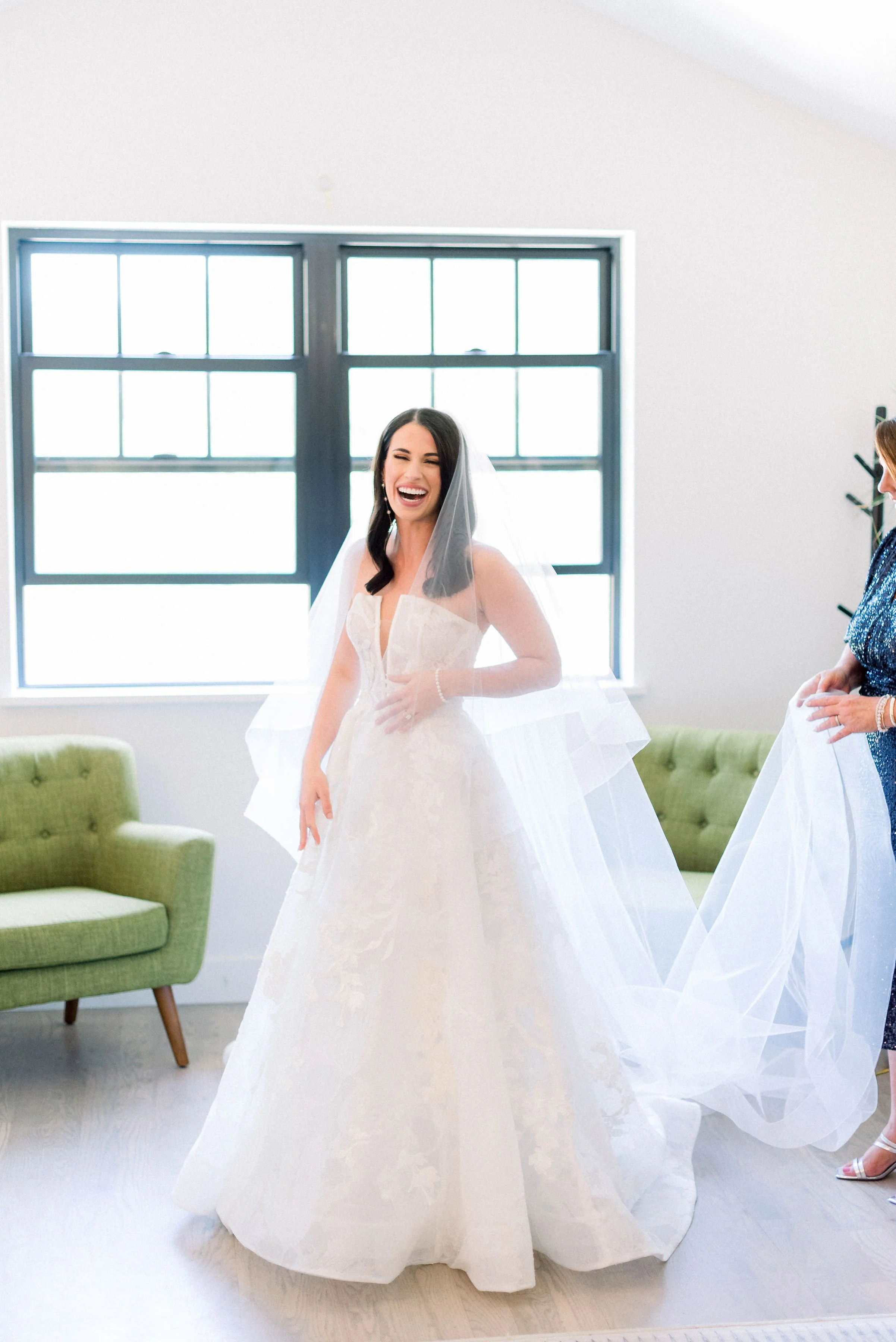 A beautiful bride in a long veil, and ballgown dress laughs for the camera