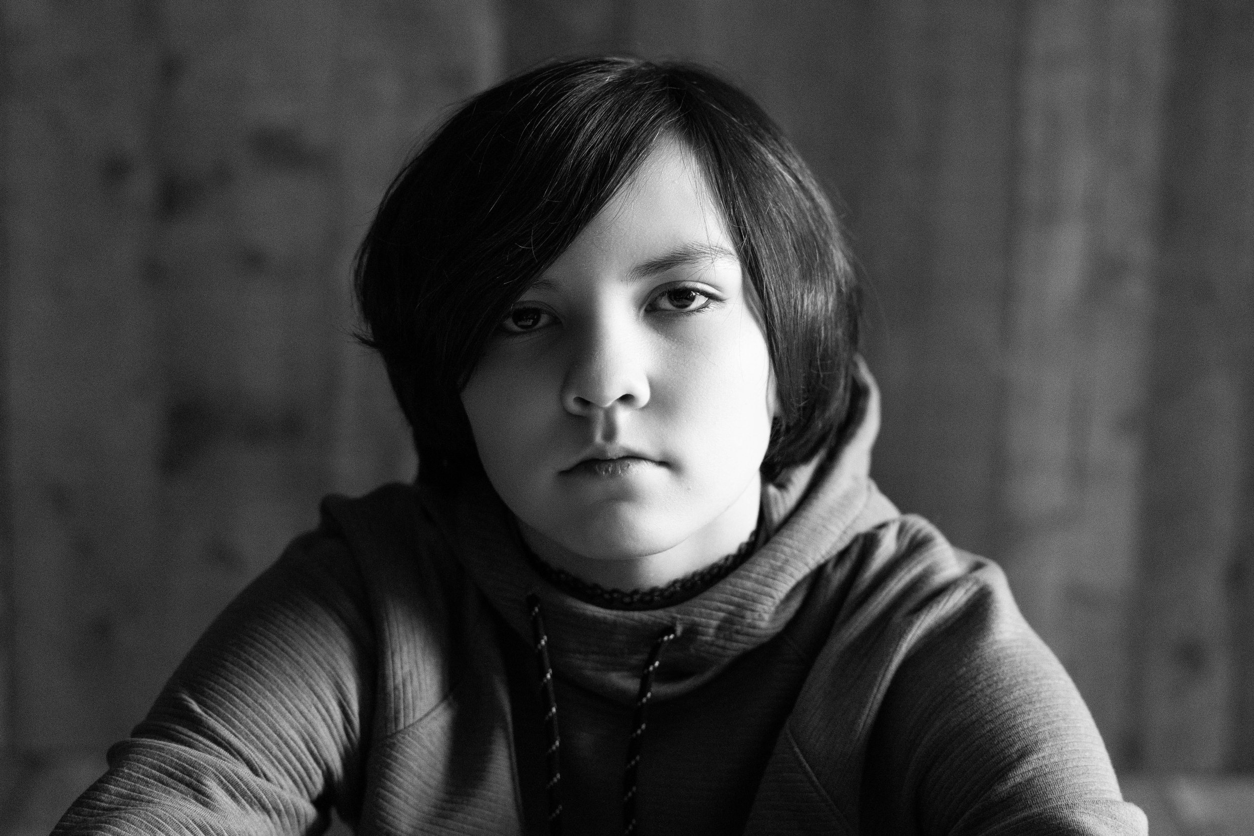 Black and white portrait of a young woman with short dark hair, wearing a hoodie and choker, looking directly at the camera with a serious expression.