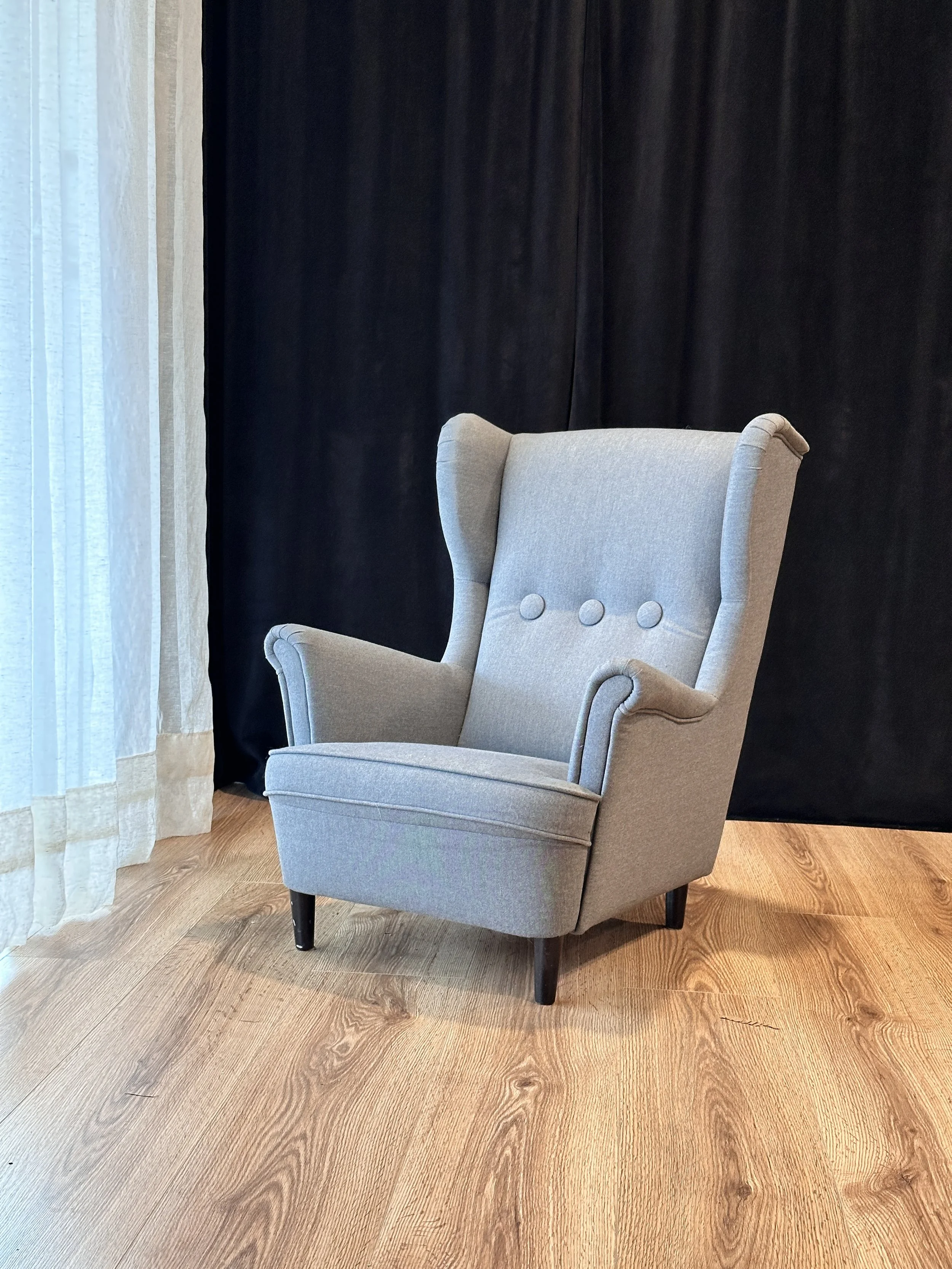 Child size gray wing back chair in front of a black curtain background