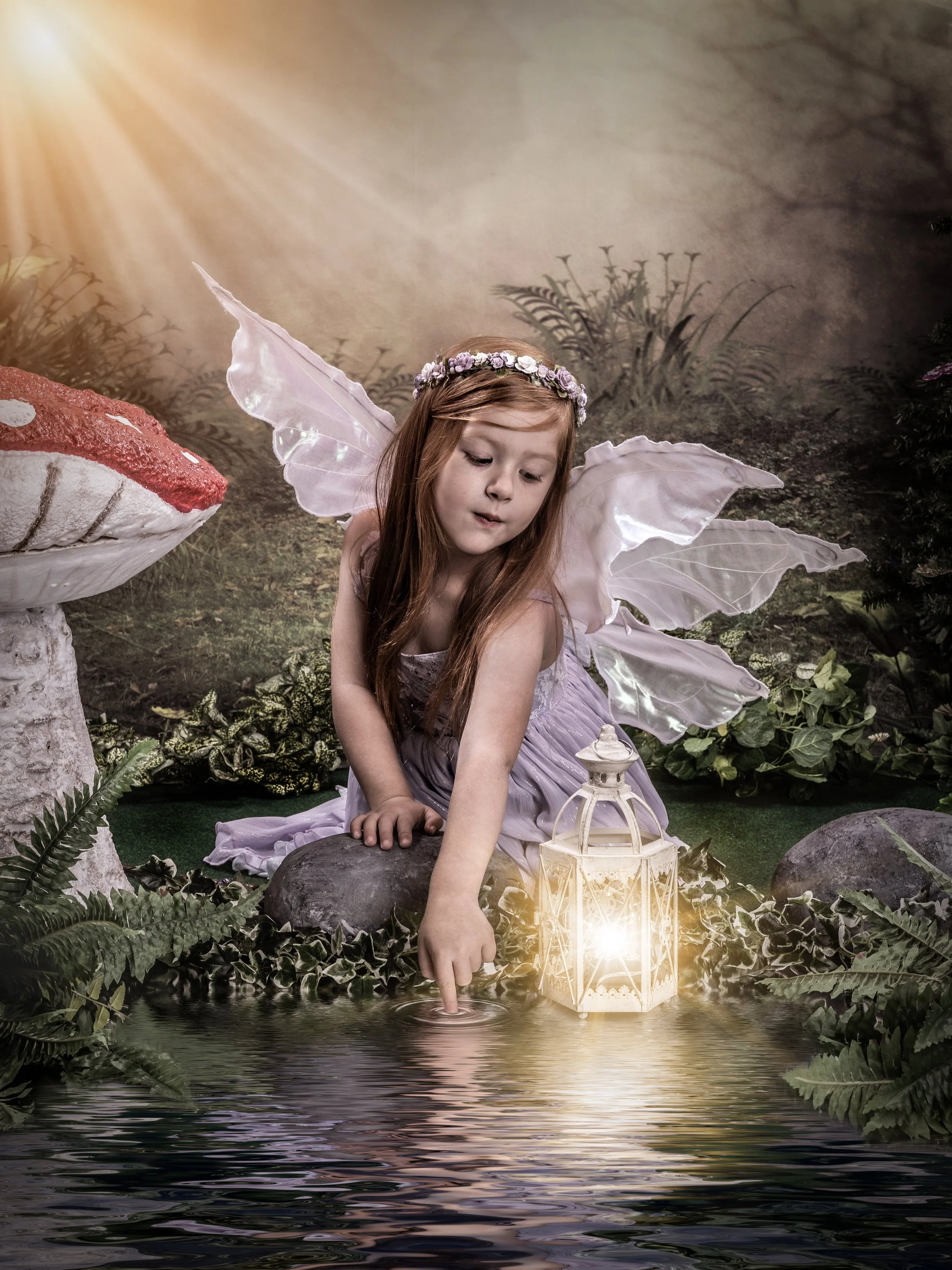 Young girl dressed as a fairy with wings and flower headband, touching a reflective water surface near a glowing lantern and large mushroom in a forest setting.