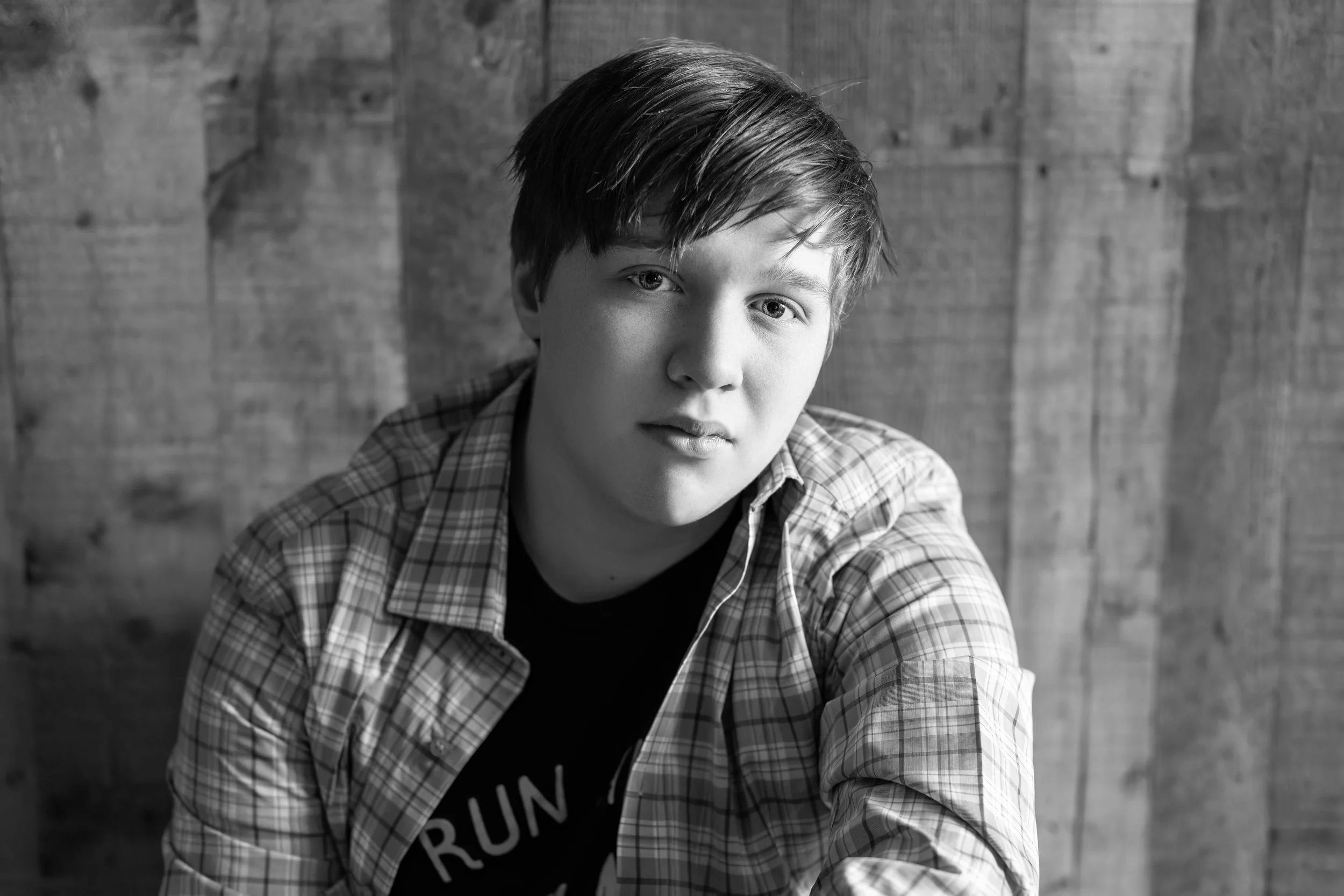 high school senior boy sitting in front of a wood wall