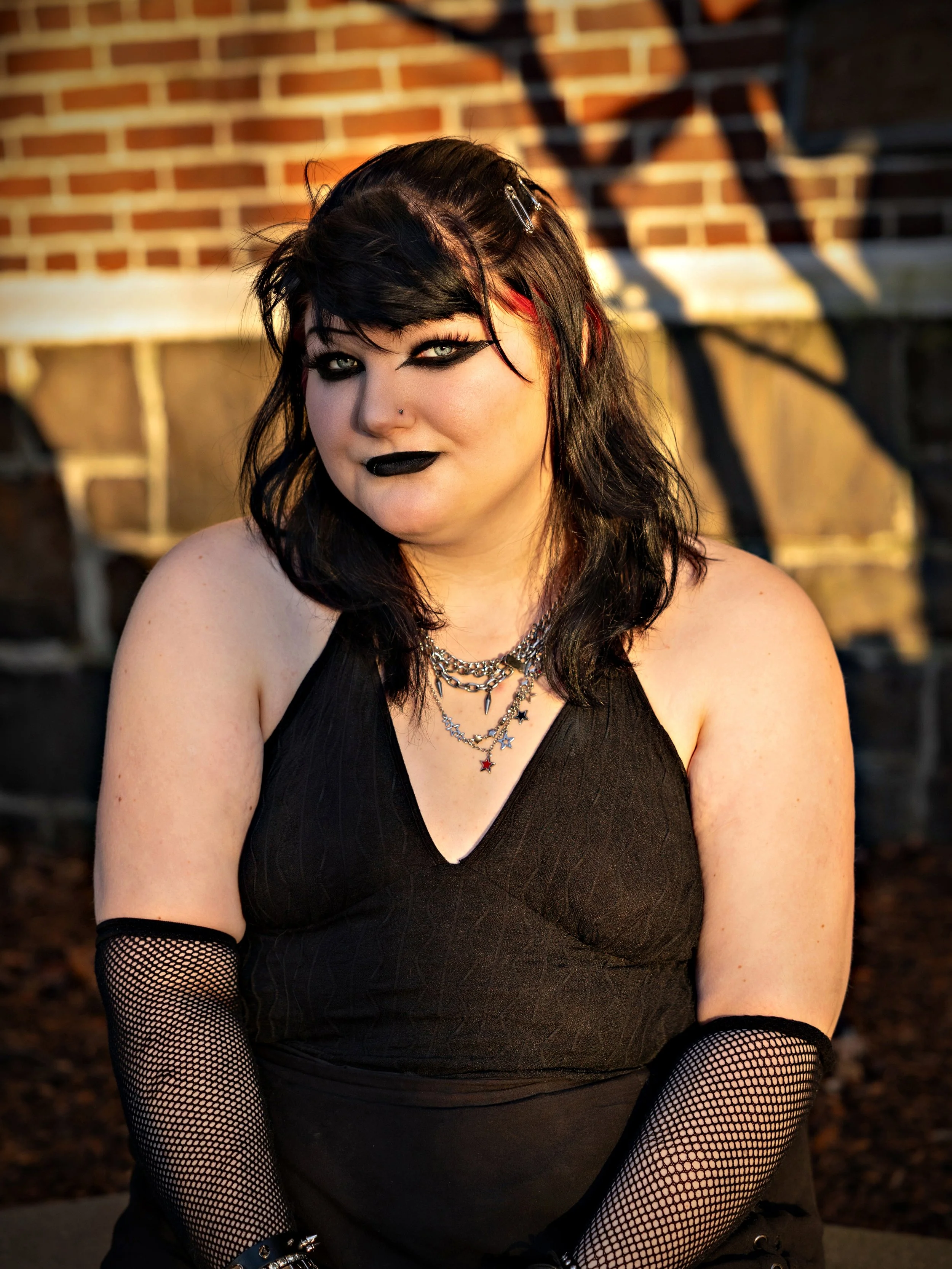 High school senior sitting in the sun in front of a brick wall