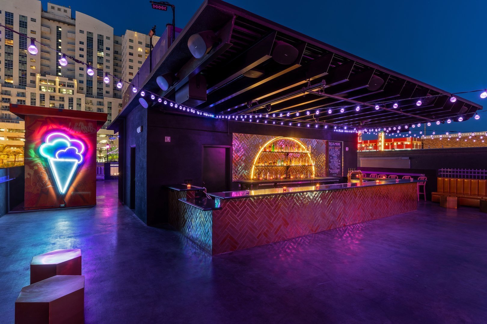 Rooftop bar with neon lights and city skyline.