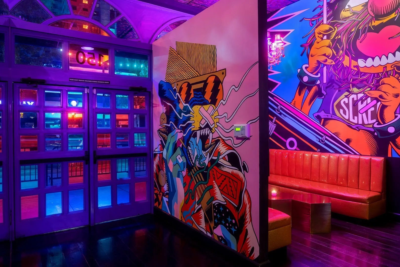 Vibrant interior with colorful murals and neon lighting, featuring a red seating area, a graphic wall art of a stylized tiger, and purple double doors.