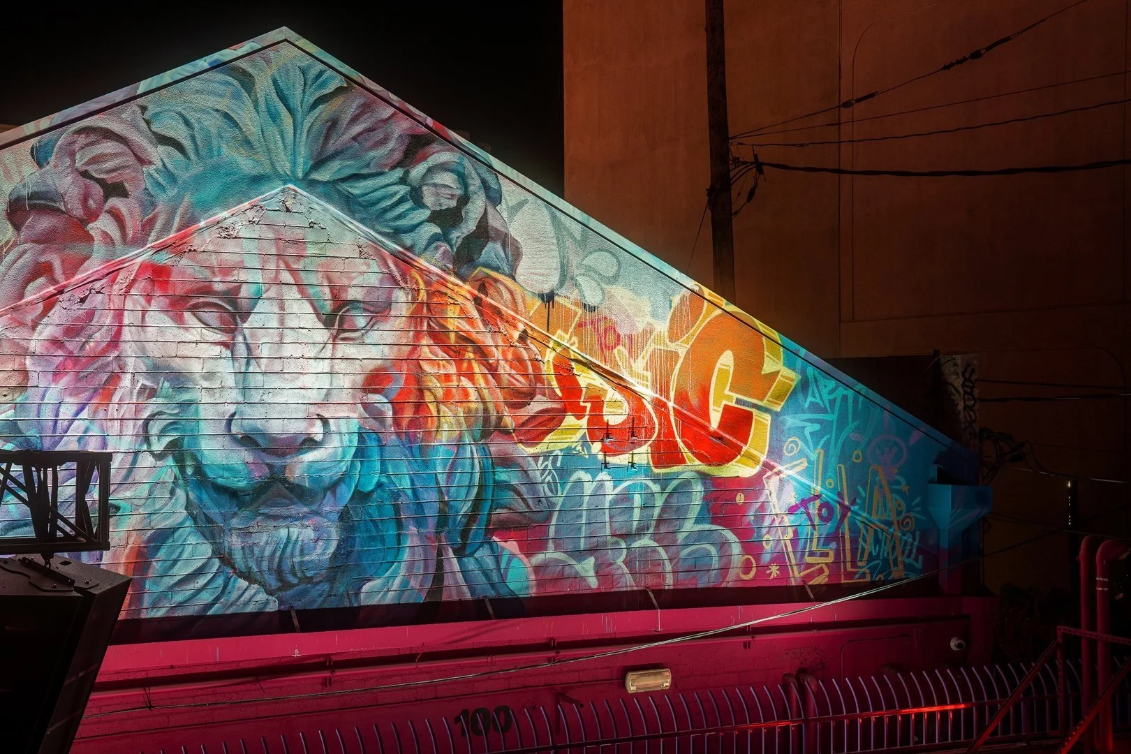 Colorful mural of a lion's face and graffiti art with the text "SIC" on a building wall at night.