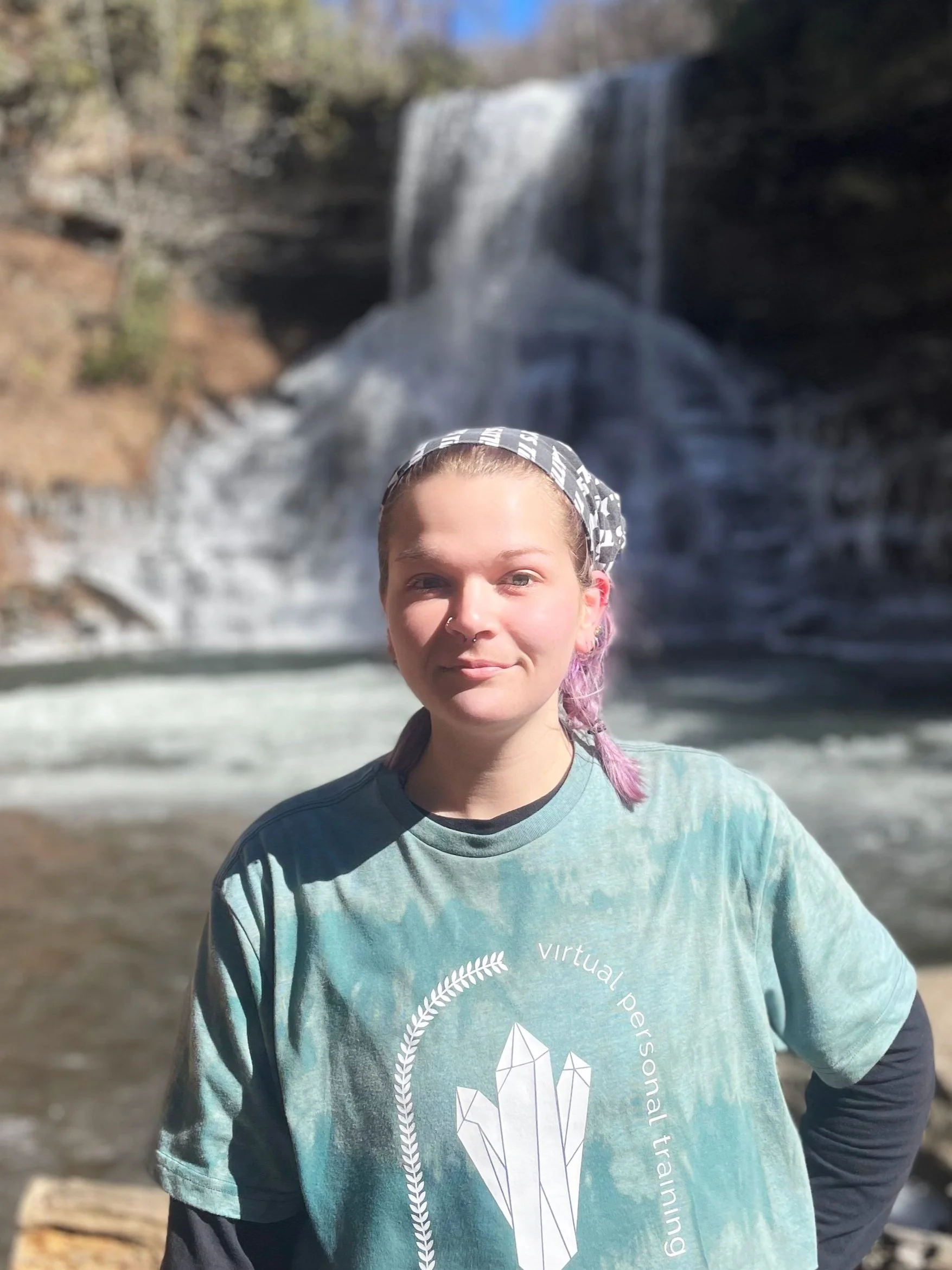 fitness coach stands smiling in front of waterfall.