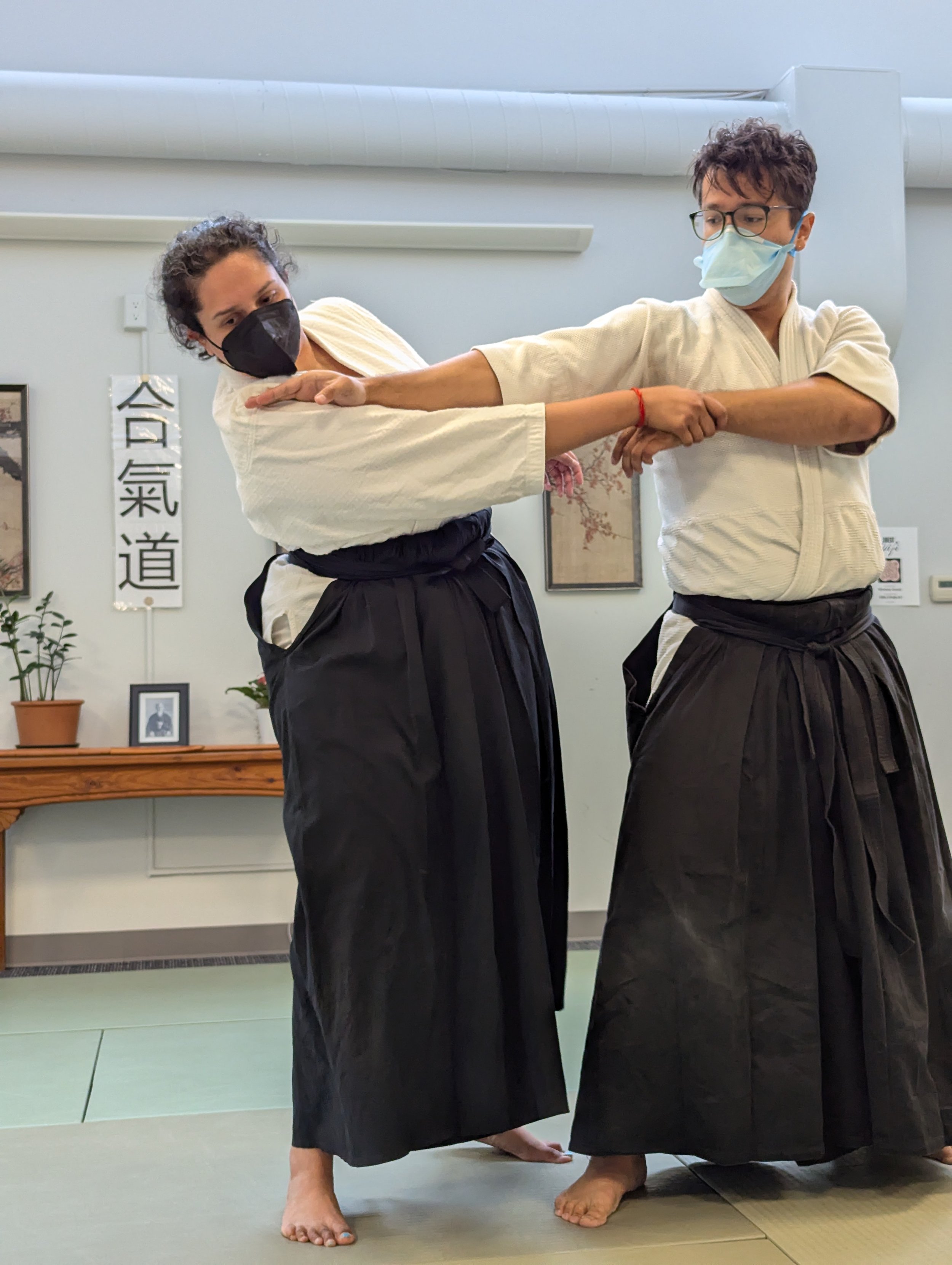 César demonstrating a detail of a technique, placing his hand on his partner's shoulder. Both parties are in keikogi and hakama.