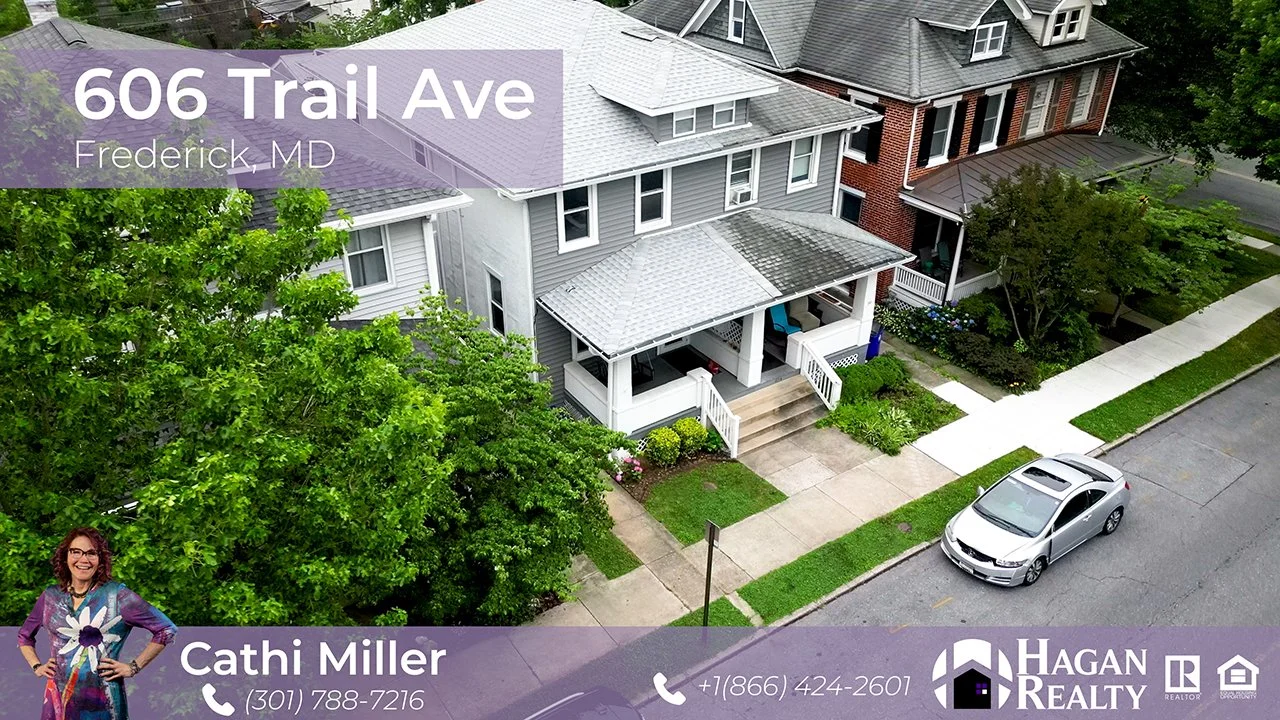 Aerial view of a residential neighborhood showing three houses on a street, one with a white exterior and a porch, another with a red brick facade, and the third with gray siding. There is a silver car parked on the street and lush green trees and lawns. Text overlays display the address 606 Trail Ave, Frederick, MD, and contact information for Cathi Miller with Hagan Realty.