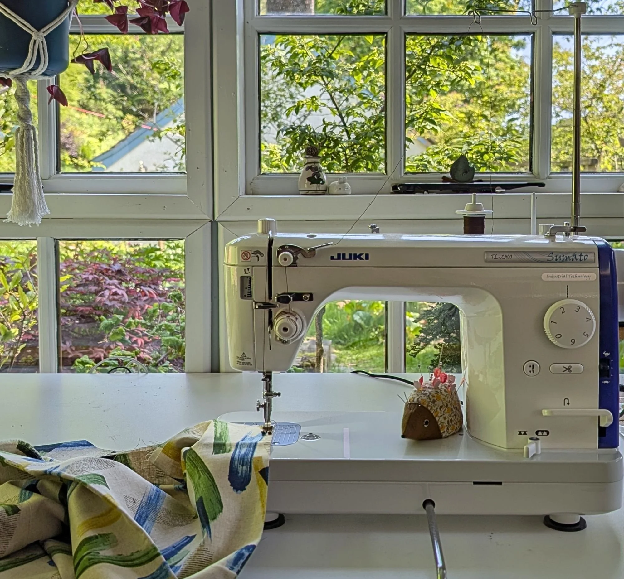 a photograph of a juki sewing machine in front of a window looking onto a lush green garden