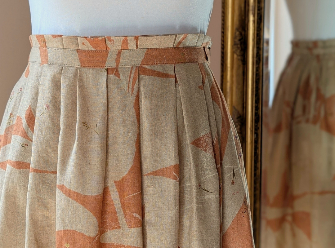 close up of a peach and cream colour skirt with a pleated waistband and a mirror behind it with a reflection of the back of the skirt.