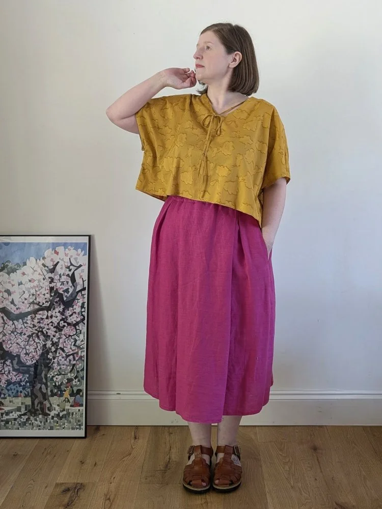 a model wearing a yellow short sleeved top and a bright pink midi length skirt