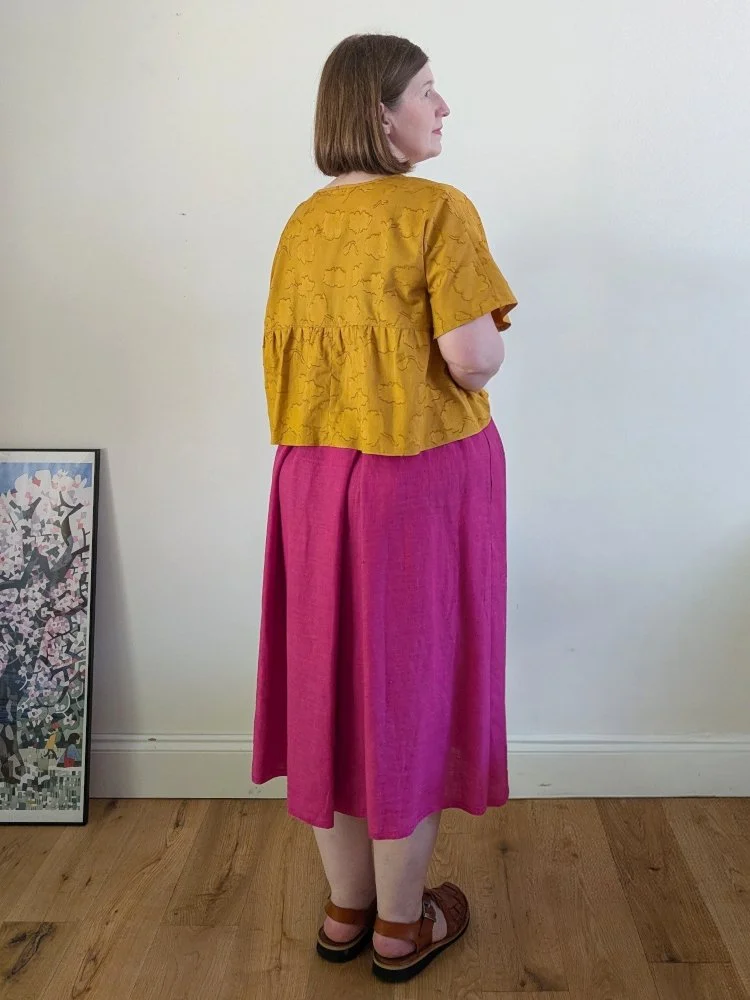 the back of a model wearing a yellow short sleeved top and a bright pink midi length skirt