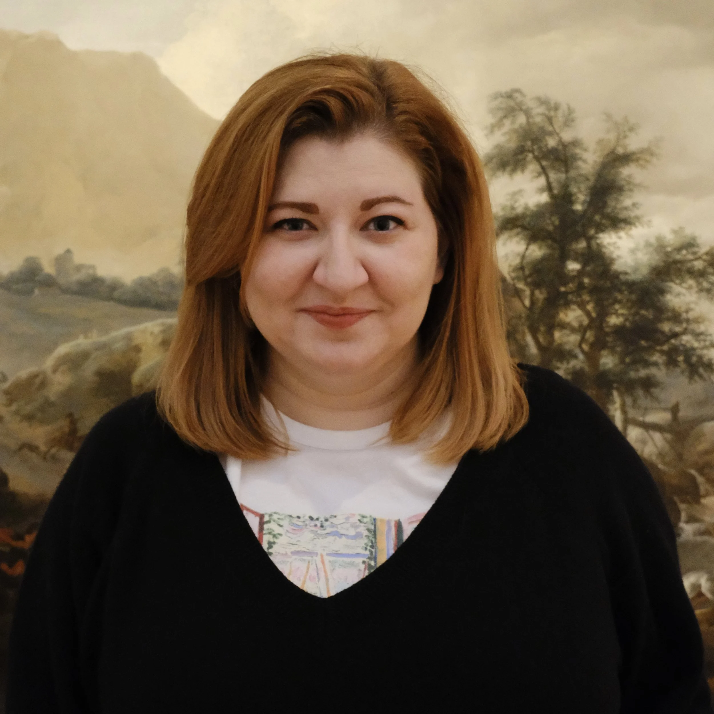 Photo of woman with short auburn hair in front of a landscape painting
