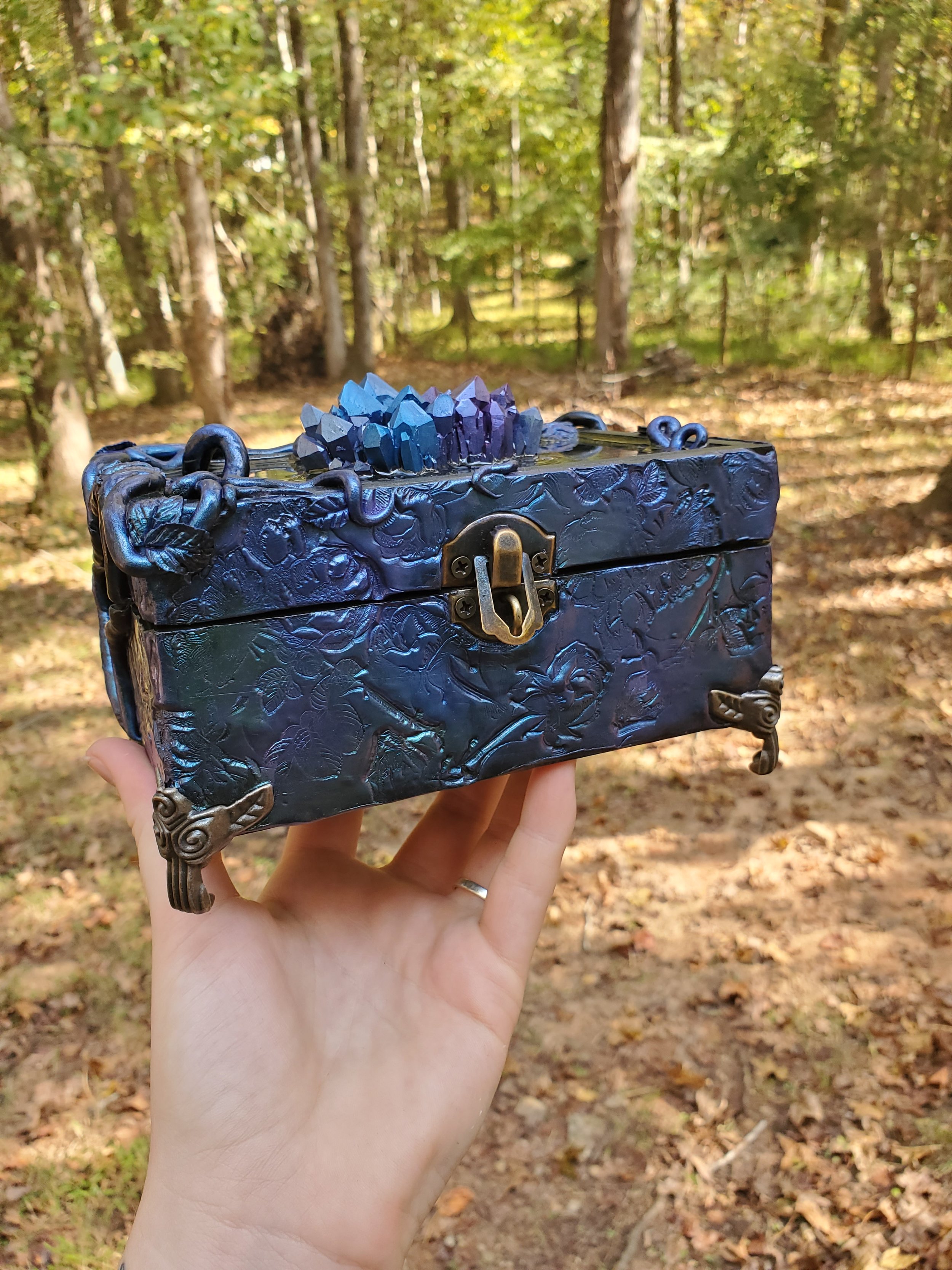 decorative dark blue box with engraved floral patterns and metal accents, topped with a cluster of purple and blue crystals
