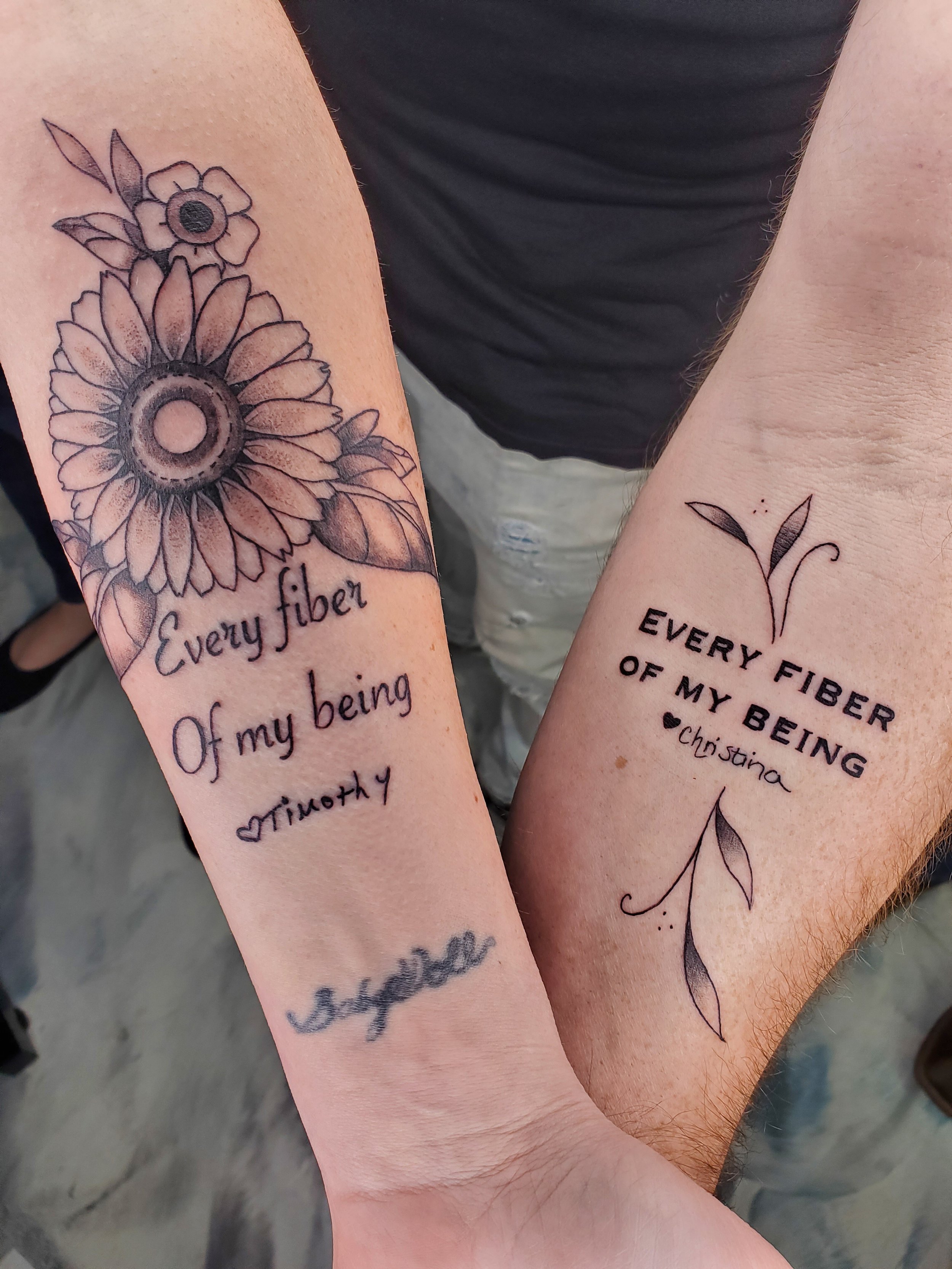 forearms  matching tattoos that say "Every fiber of my being" with a floral and leaf design, one with a sunflower and the other with a smaller flower