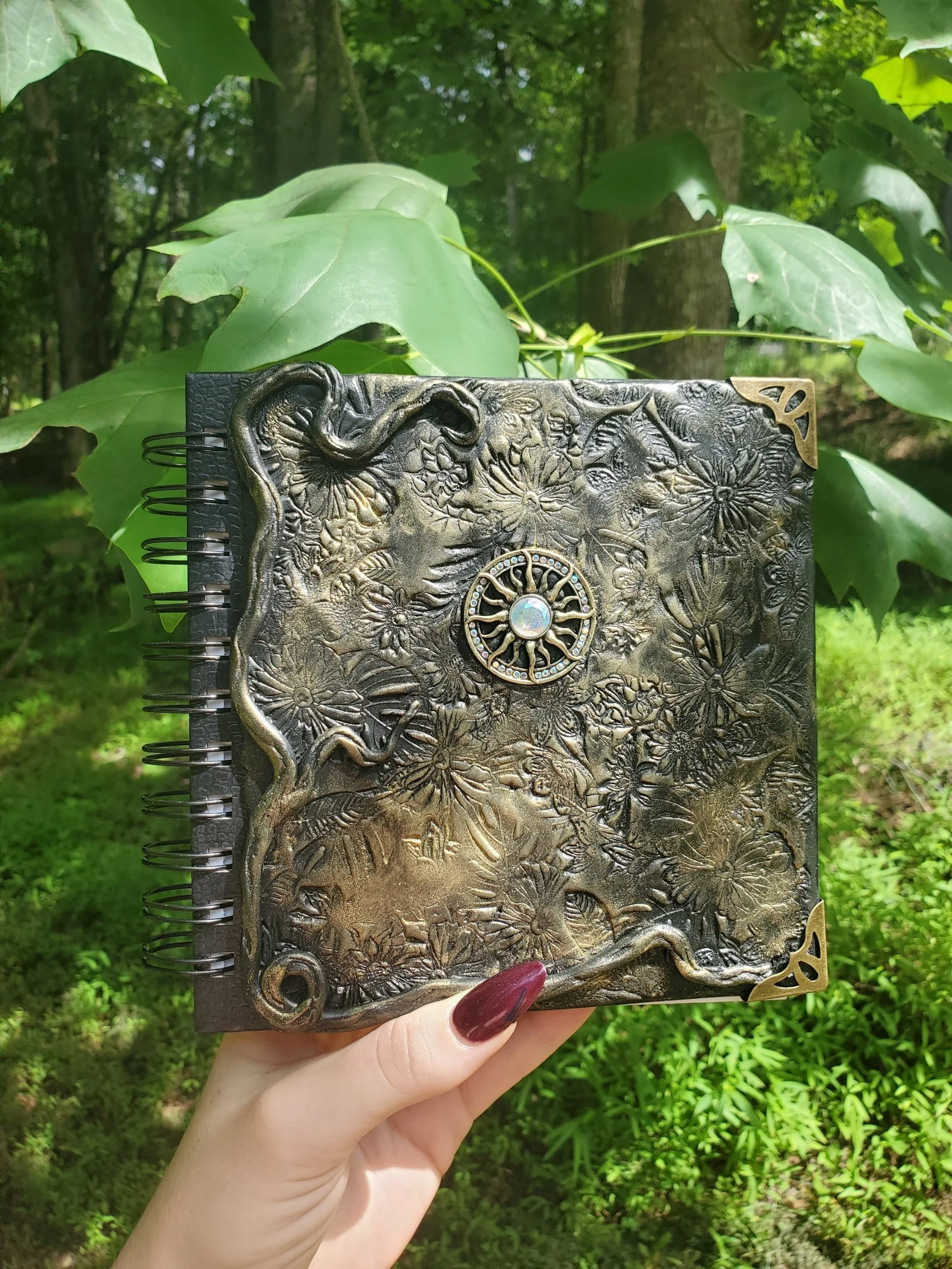 A decorative, embossed clay notebook with floral designs, featuring a circular charm in the center.