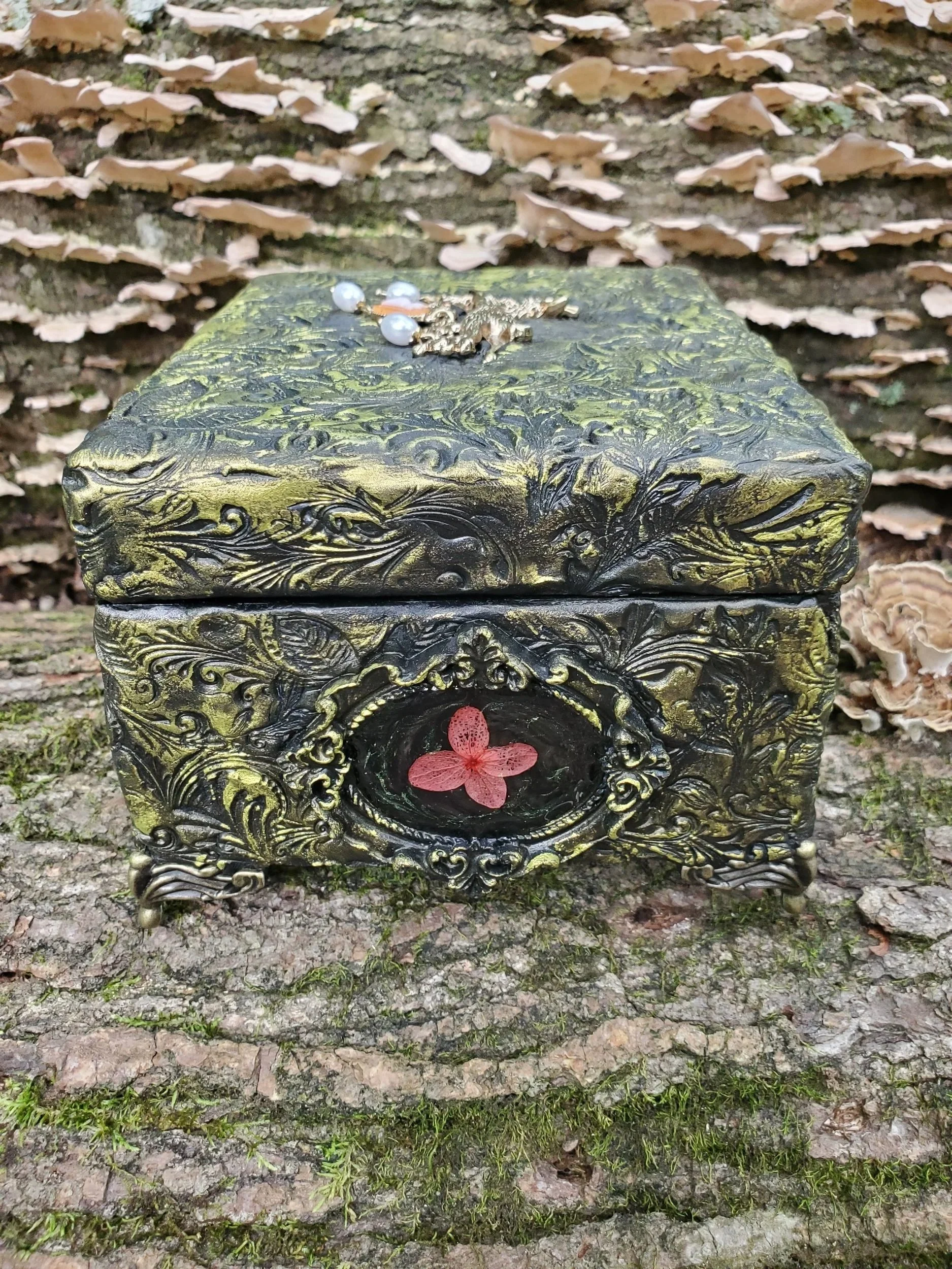 Ornate black and gold decorative jewelry box with a red flower decoration with metal accents and metallic exterior.