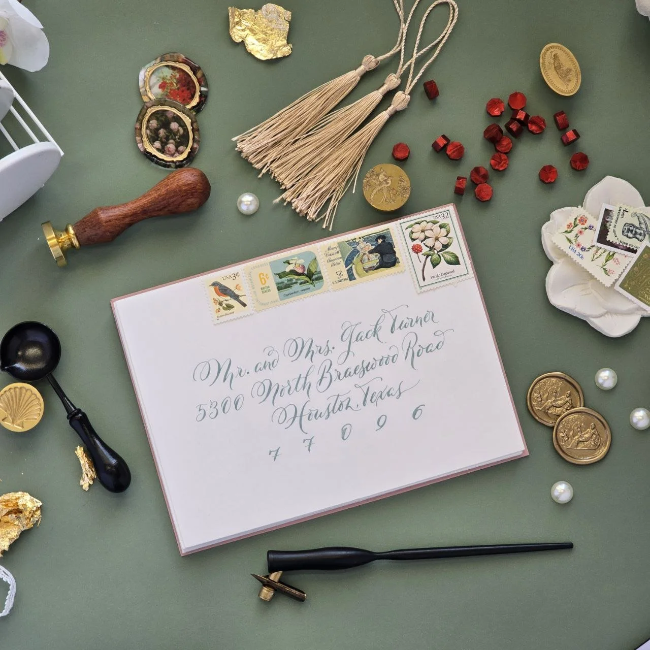 Envelope with decorative stamps, calligraphy address, and wax seal materials on a green surface.