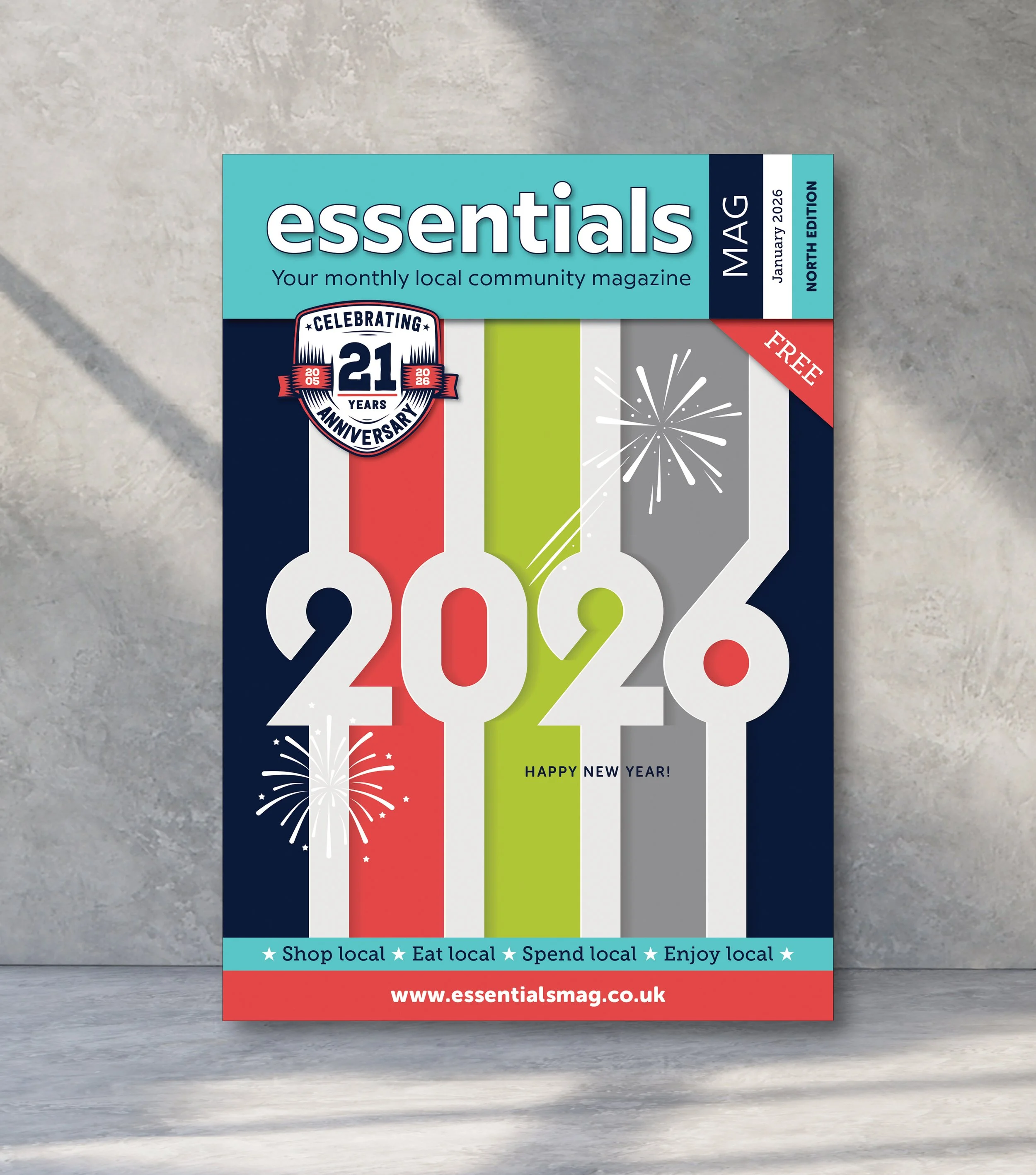 Front page of the January 2026 issue of Essentials magazine, celebrating its 21st anniversary, with colorful vertical stripes, fireworks, and the headline 'Happy New Year!'.