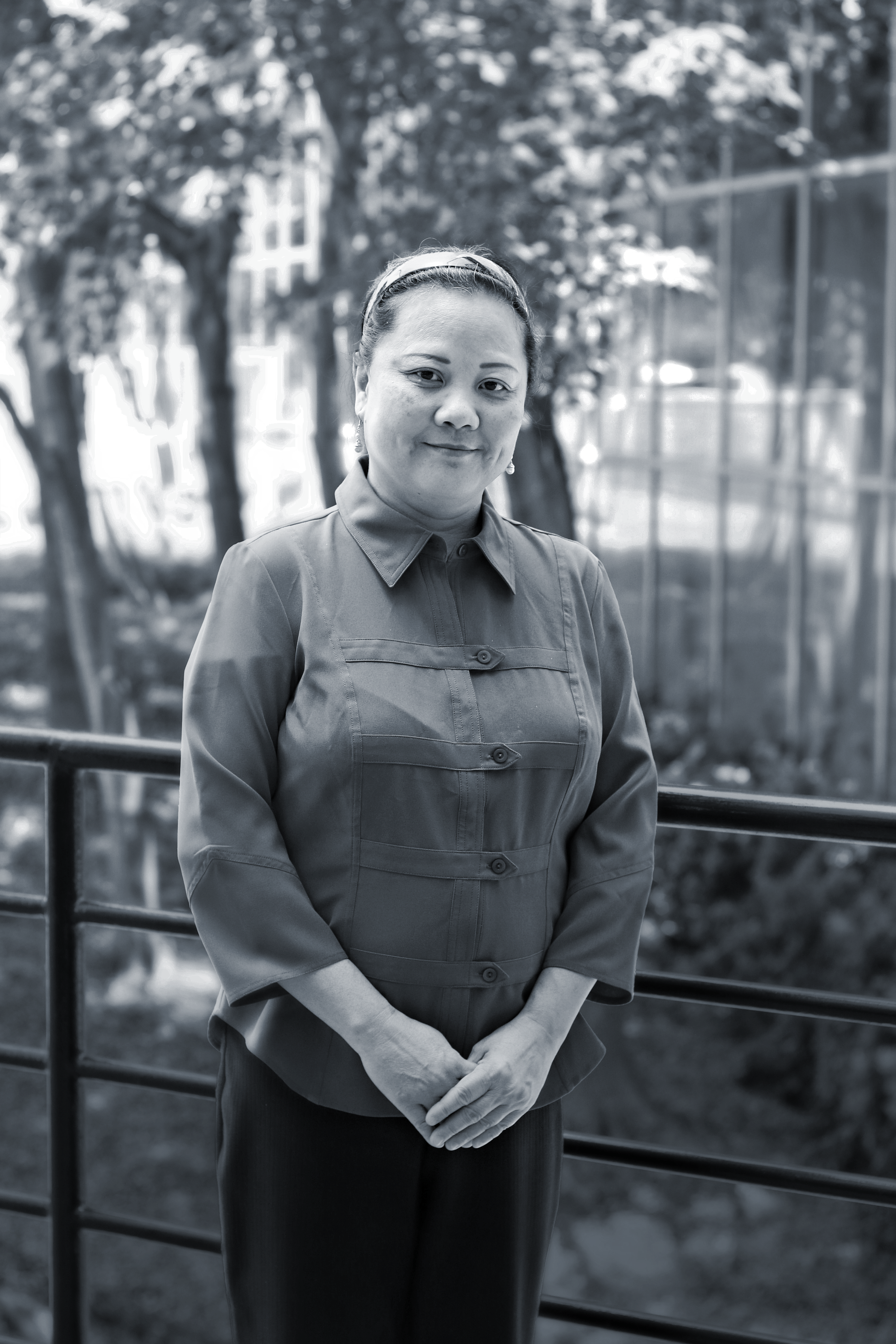 Black and white photo of a woman smiling outdoors with trees in the background