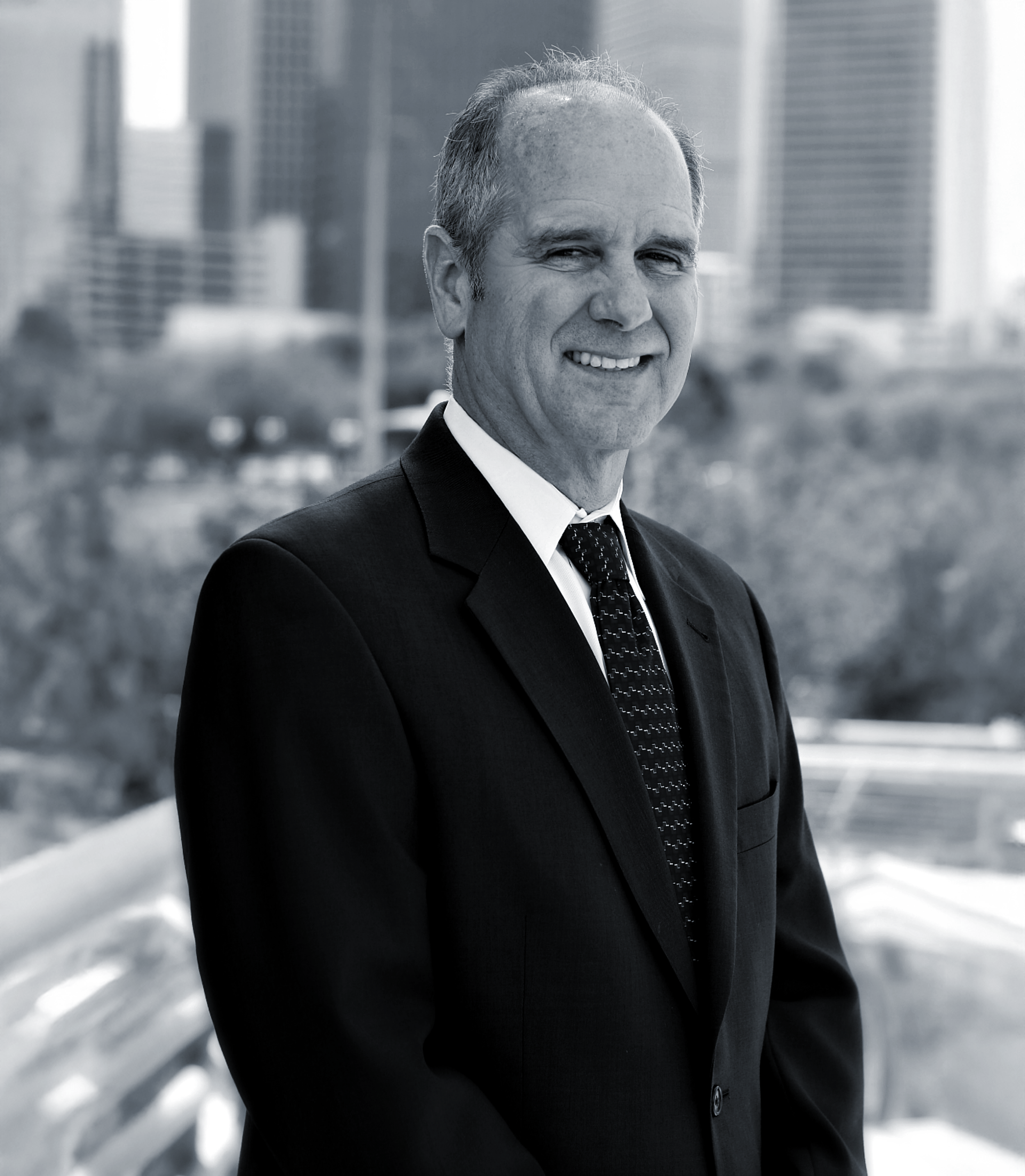 Portrait of a middle-aged man in a business suit smiling, with a blurred cityscape background.
